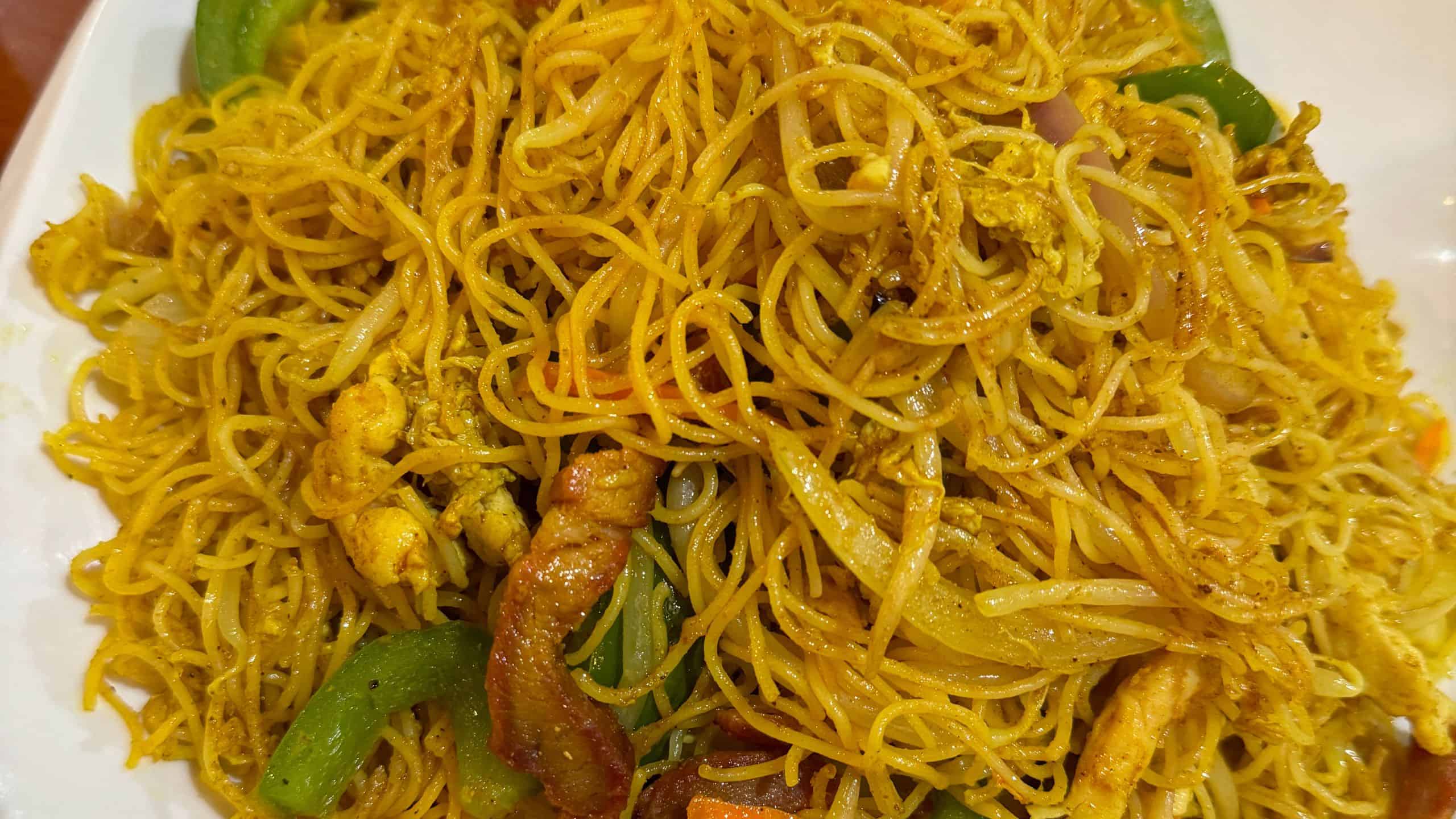 A close-up of stir-fried noodles with chicken, green bell peppers, onions, and bean sprouts on a plate.