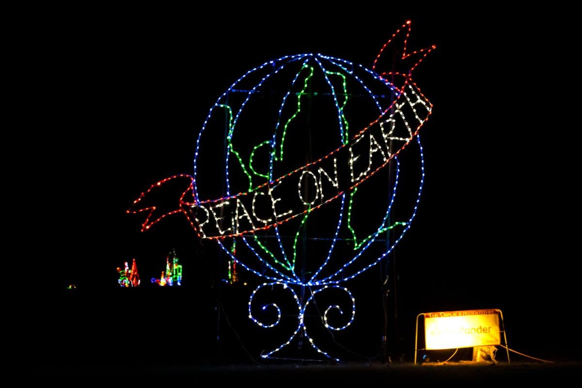 Colored lights form a globe with a red ribbon reading "Peace on Earth" displayed at night; a lit sign is visible on the lower right.