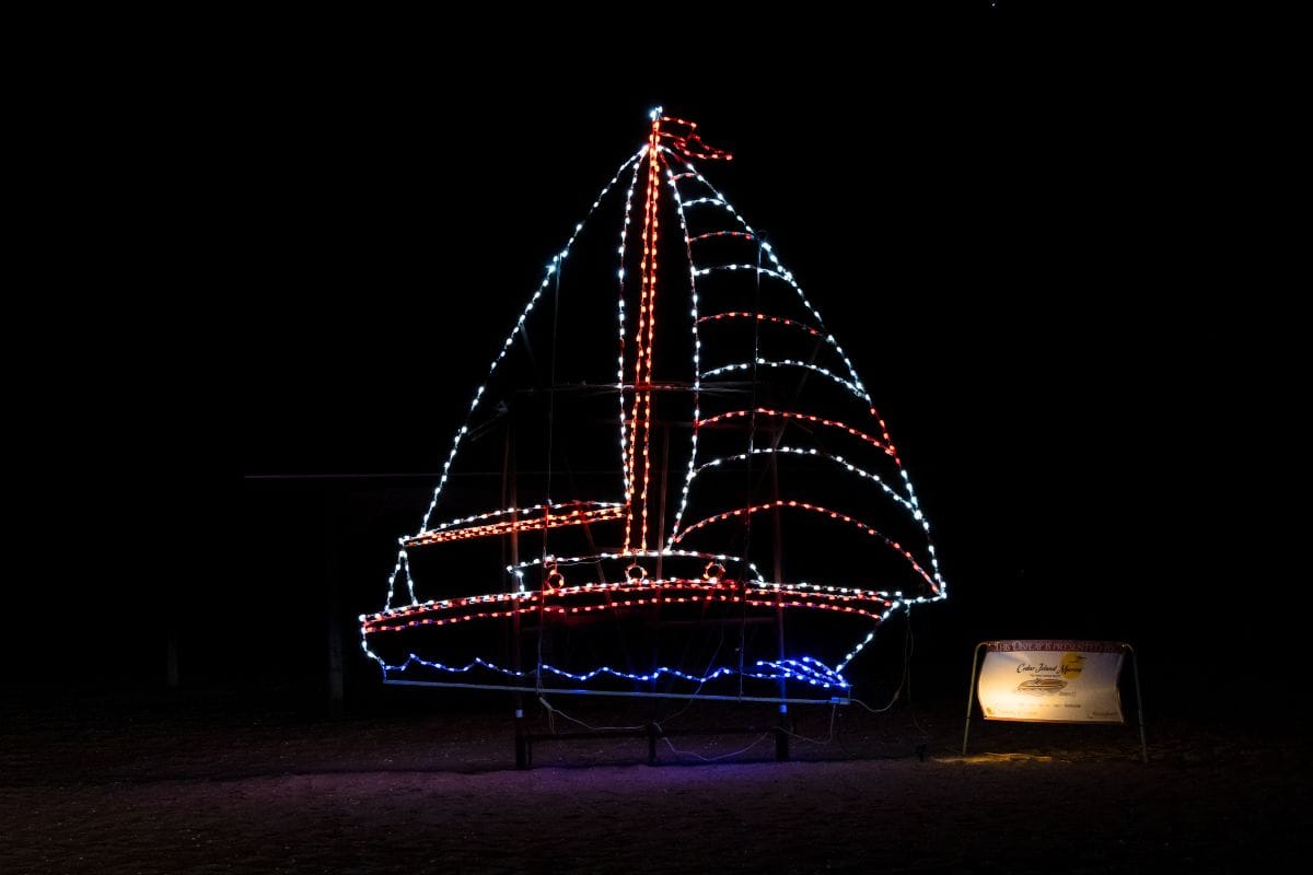 A sailboat-shaped light display with red, white, and blue lights is illuminated at night. A lit sign is visible to the right of the display.