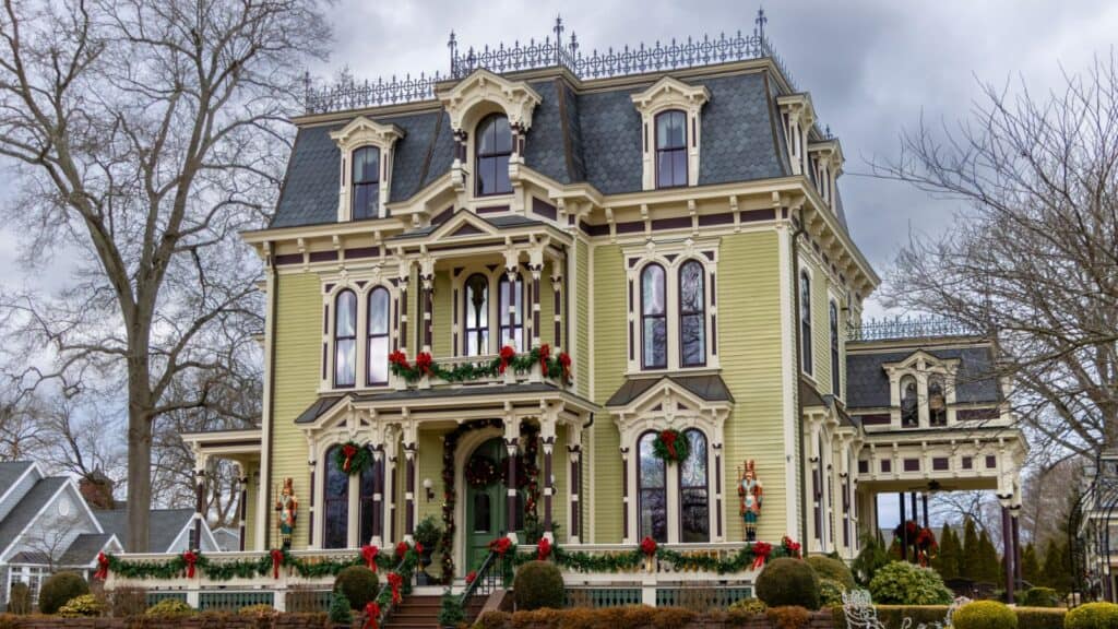 Victorian-style house with ornate details, decorated with red bows and wreaths for the holidays, set against a cloudy sky.