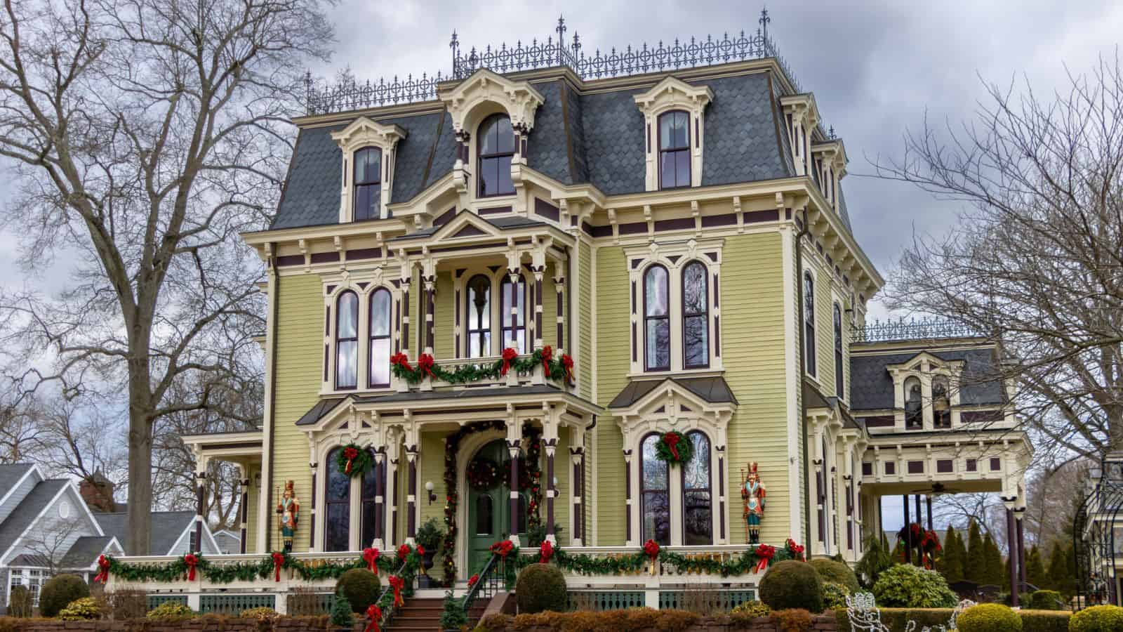 Victorian-style house with ornate details, decorated with red bows and wreaths for the holidays, set against a cloudy sky.