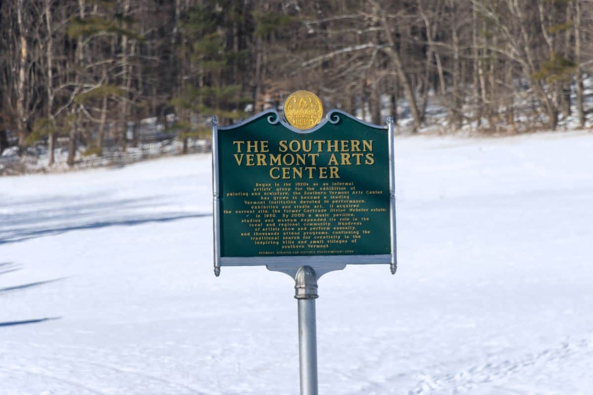 A green historical marker sign for The Southern Vermont Arts Center stands in a snowy field with leafless trees in the background.