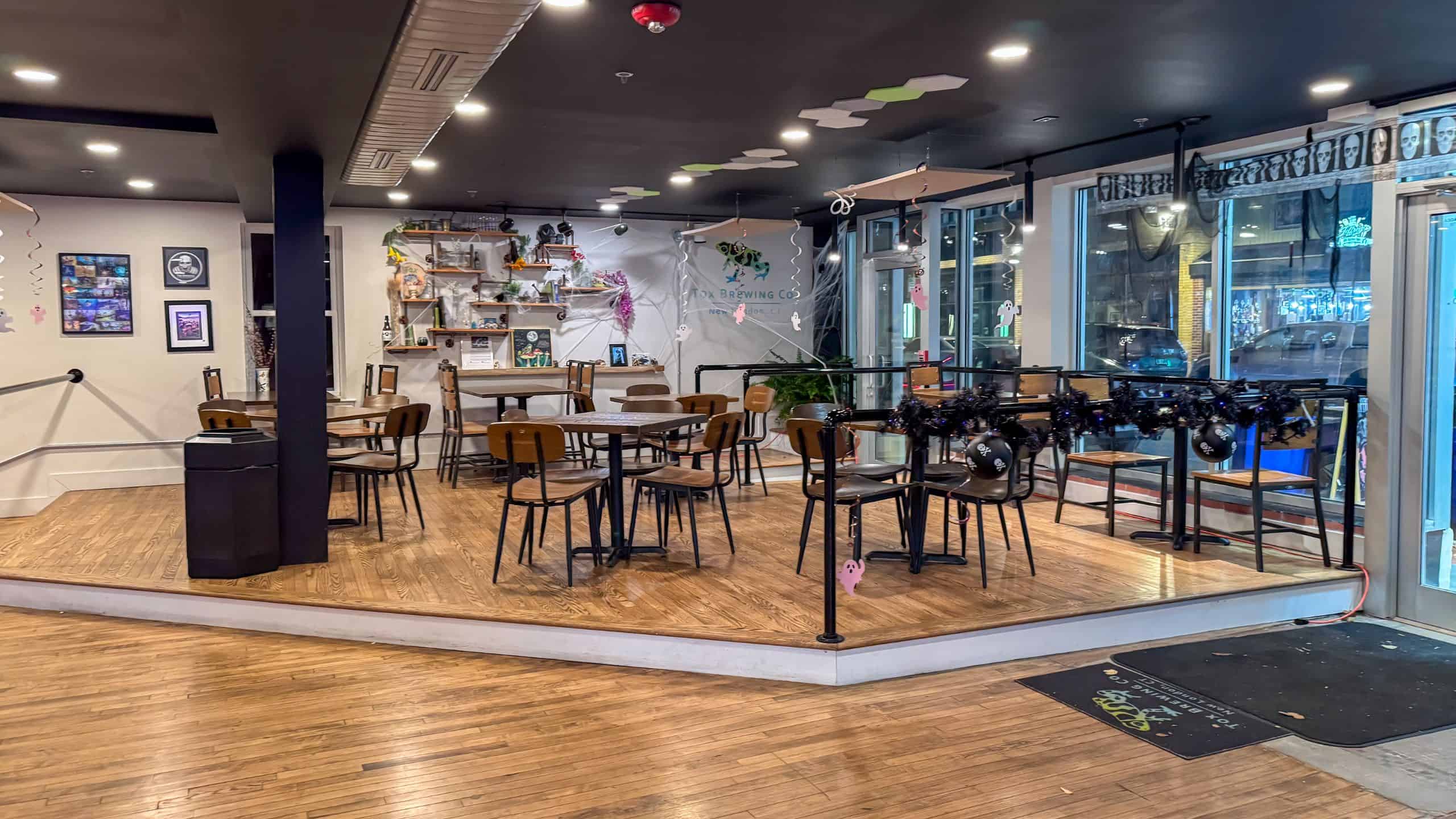 A cozy, modern café interior with wooden floors, empty tables and chairs, a decorated counter, and large windows letting in natural light.