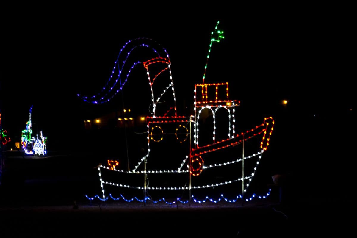 A boat outlined in colorful holiday lights, with blue lights for water, displayed at night against a dark background.