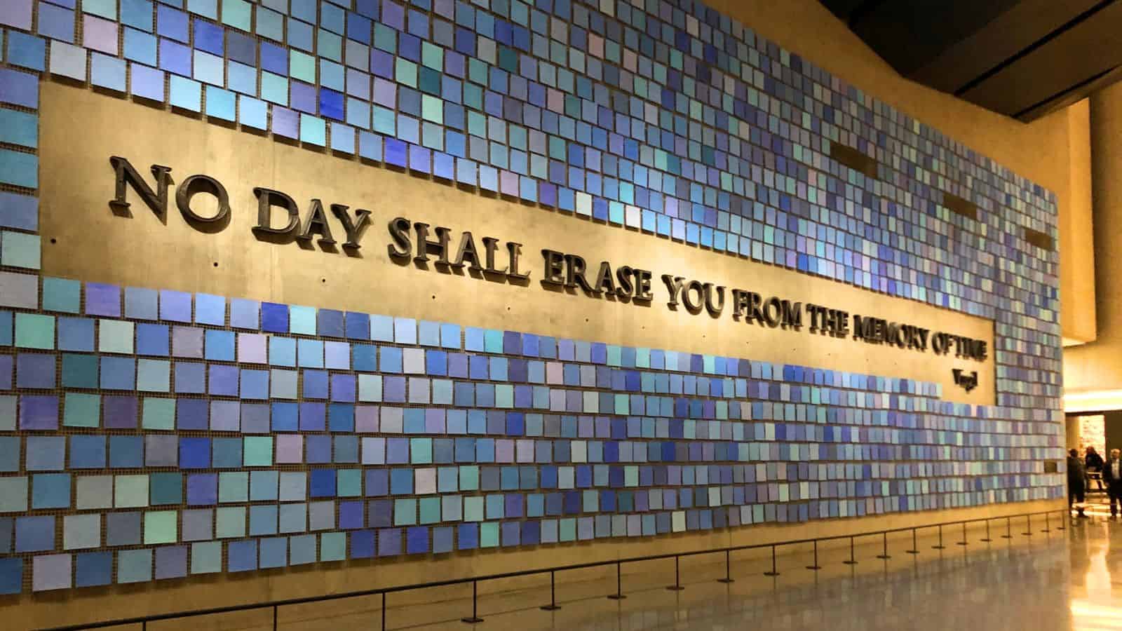 A large memorial wall displays the quote "No day shall erase you from the memory of time" surrounded by a mosaic of blue tiles.