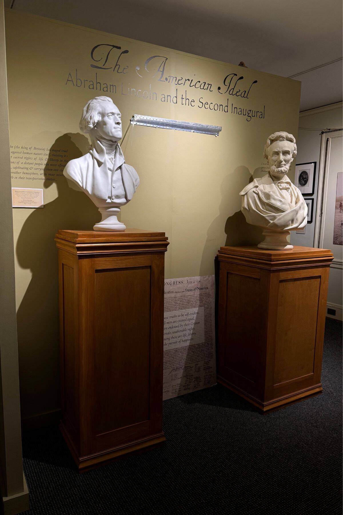 Two white marble busts of Abraham Lincoln and another man are displayed on wooden pedestals in a museum exhibit titled "The American Ideal: Abraham Lincoln and the Second Inaugural.