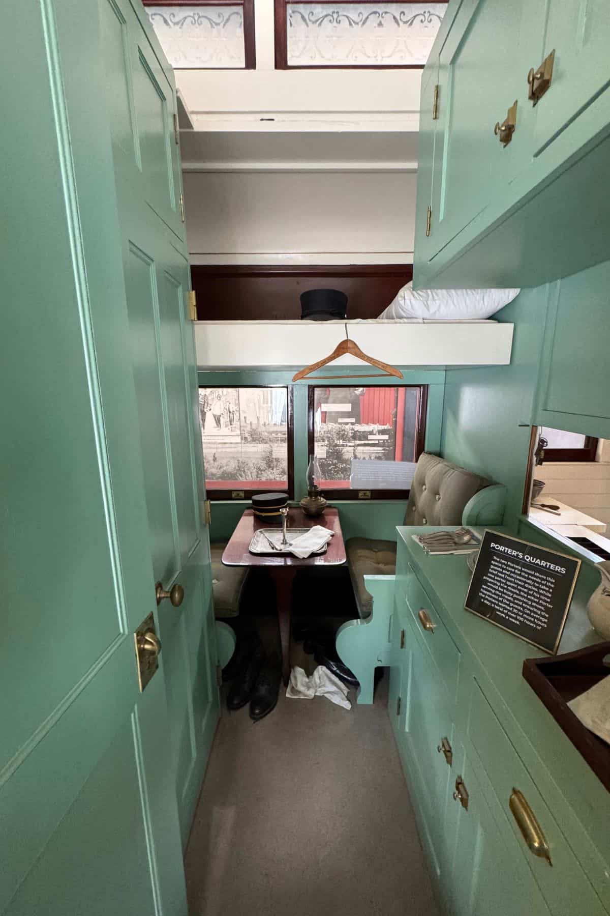 Narrow train compartment with mint green cabinetry, bunk beds, a small dining table, and personal items on display, including a sign labeled "Porter's Quarters.