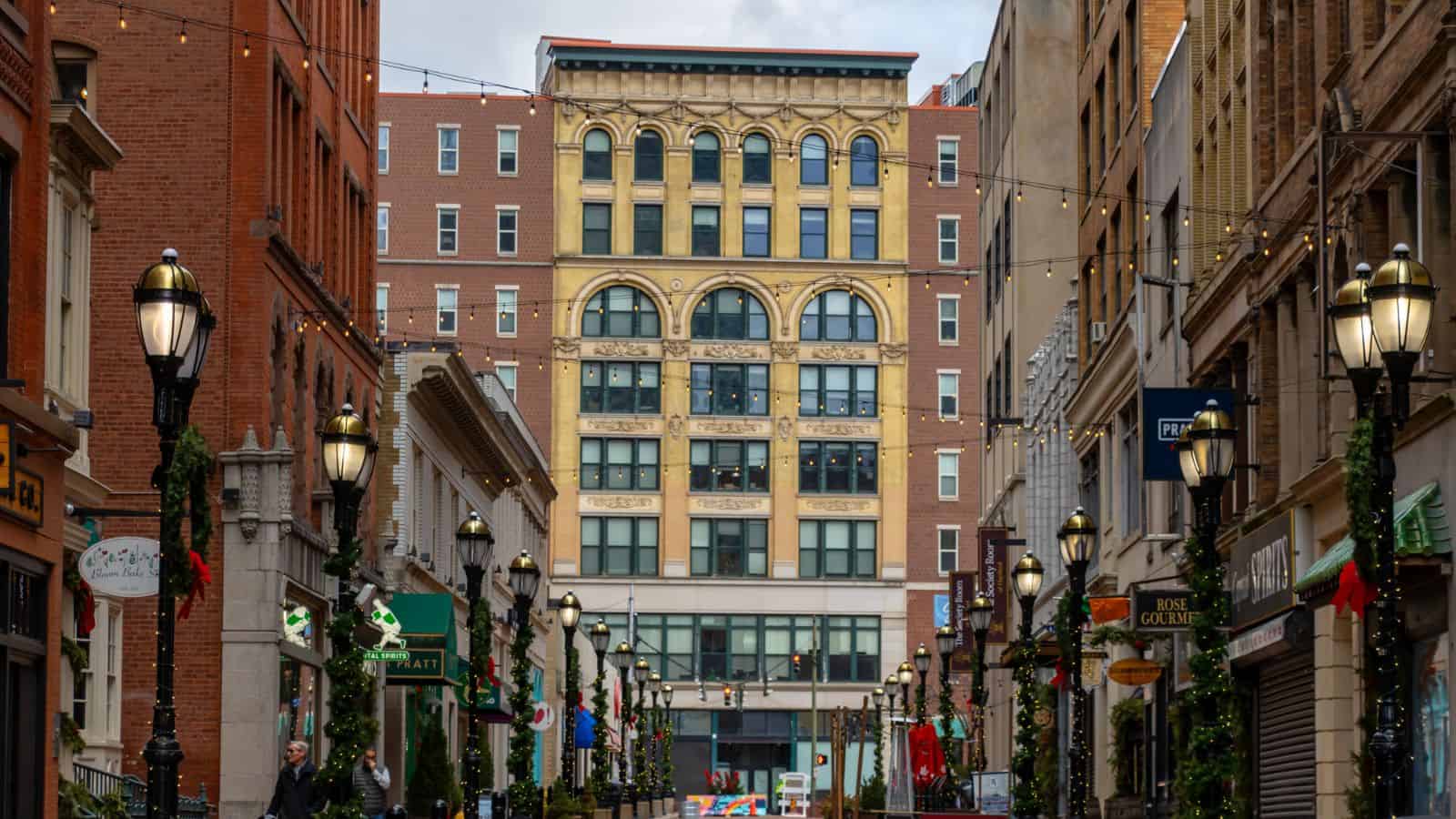A decorated pedestrian street lined with shops and lampposts leads to a tall, ornate building in an urban setting.