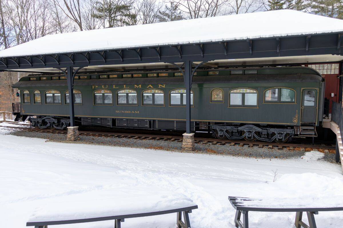 A vintage Pullman train car labeled "Sunbeam" is displayed under a metal canopy, surrounded by snow and trees.