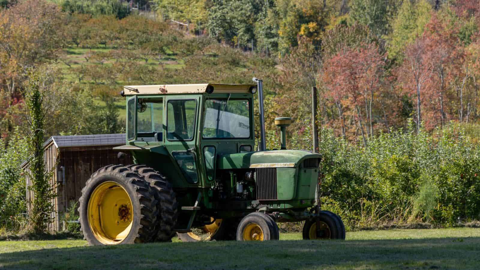 A green tractor with yellow wheels is parked on grass in front of a small shed, with trees and foliage in the background.