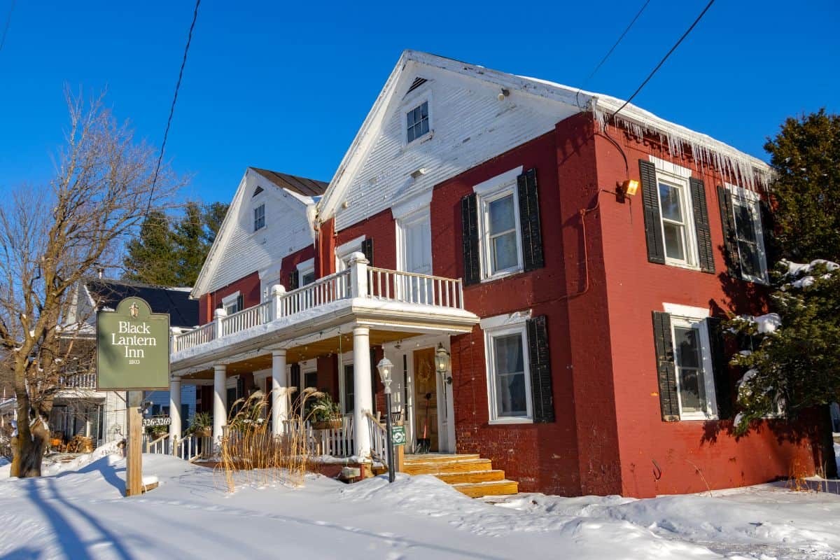 A two-story red and white building in winter houses the Black Lantern Inn, with snow covering the ground and icicles hanging from the roof.