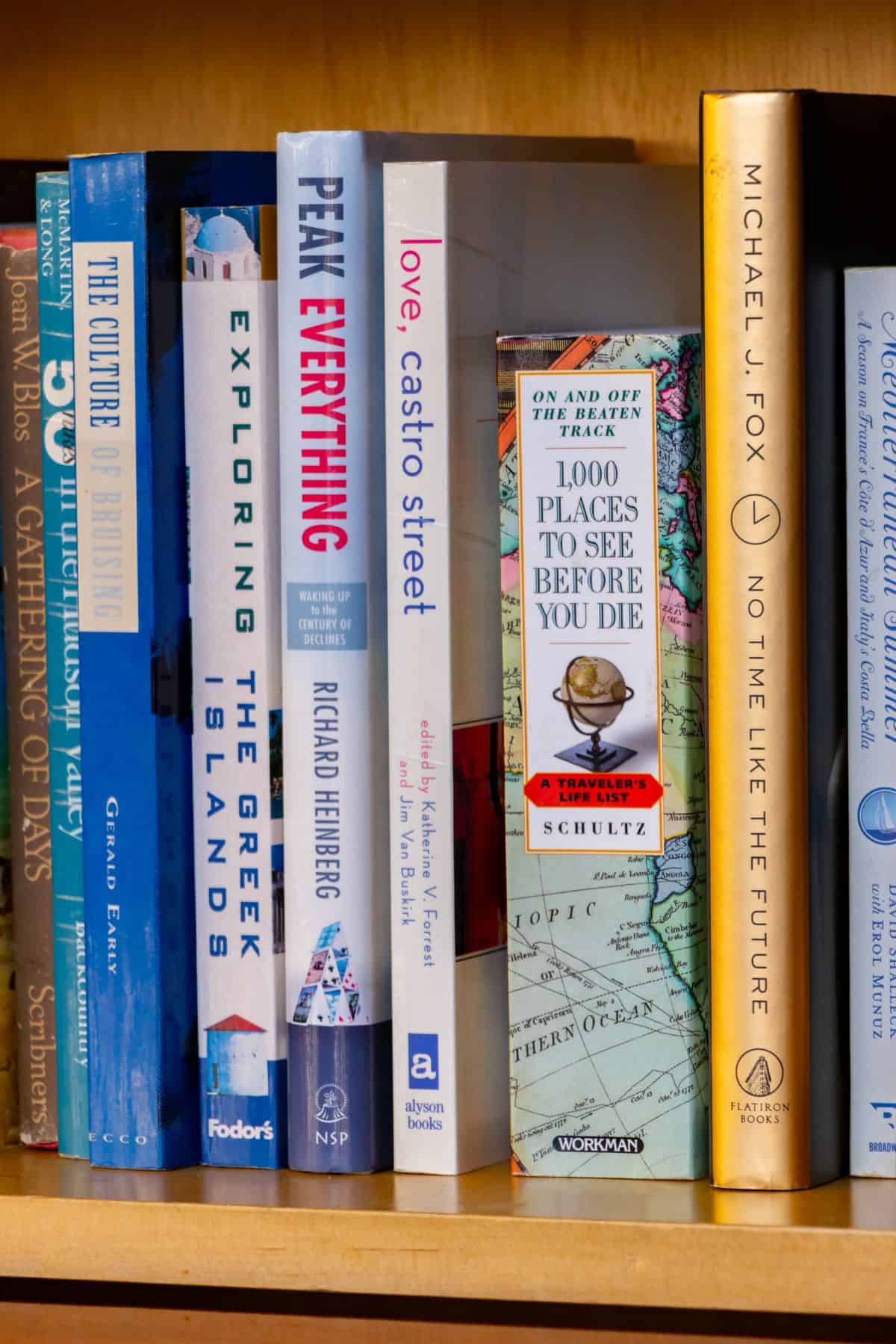 A close-up of a bookshelf displaying various books, including travel guides, memoirs, and nonfiction titles arranged upright.