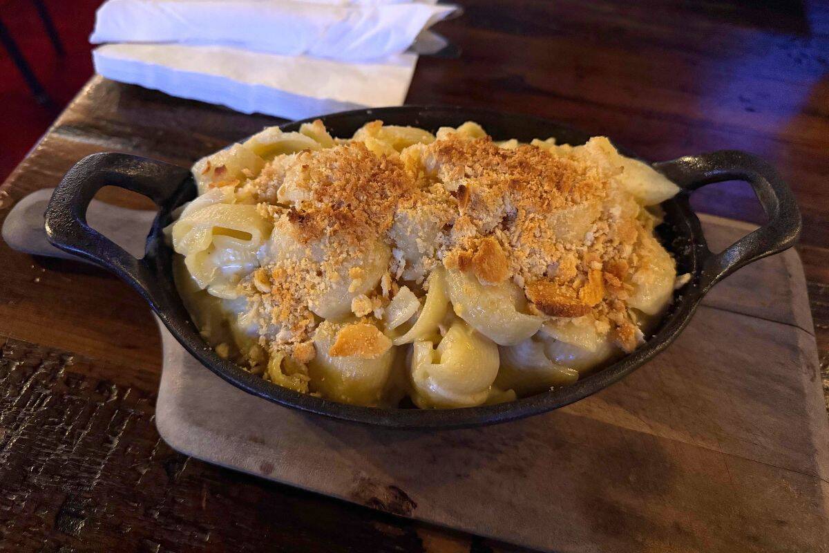 A cast iron dish filled with baked macaroni and cheese topped with golden breadcrumbs, set on a wooden board.