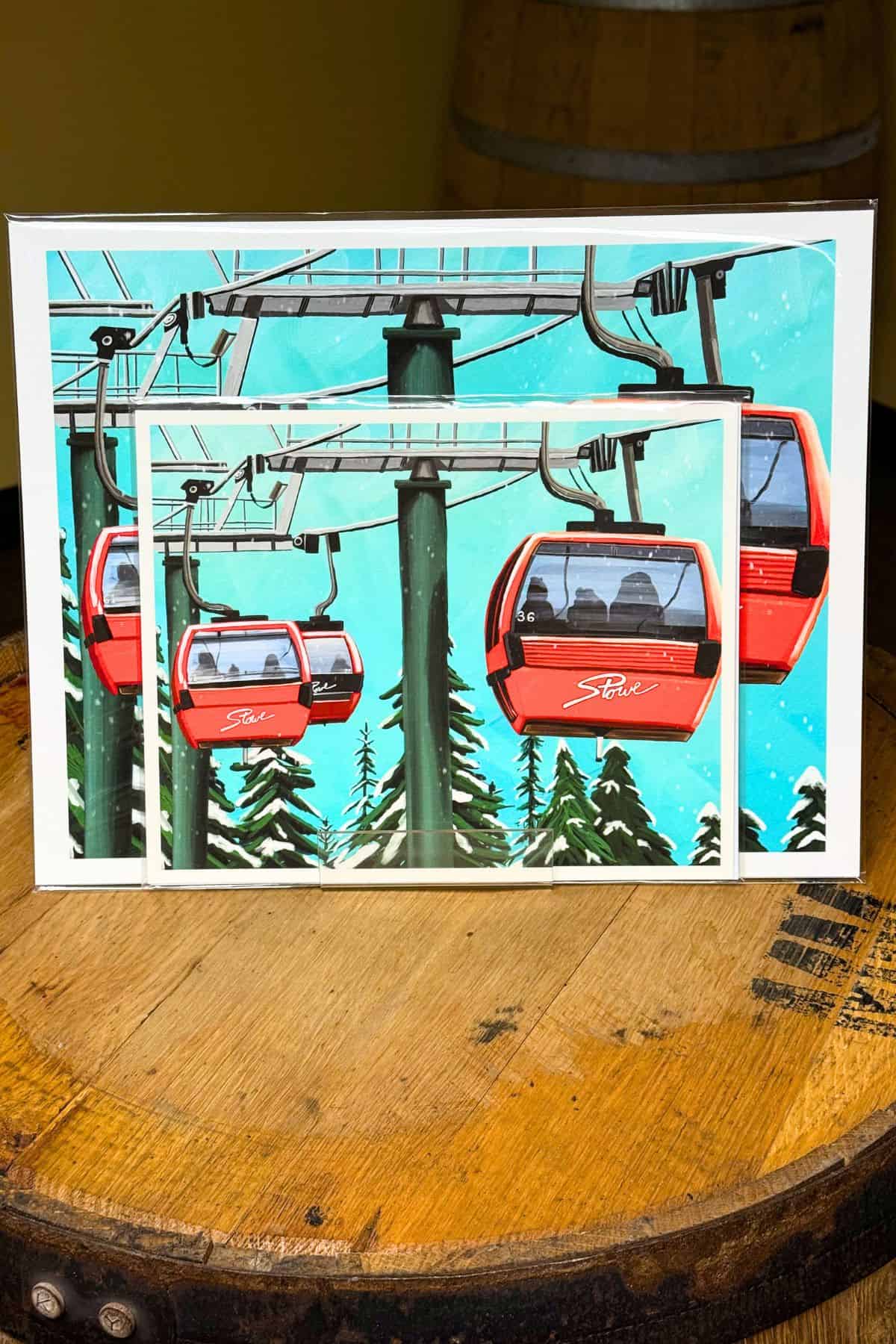 A framed print of red gondolas on a ski lift hangs above a wooden barrel; the print features snow, trees, and blue sky in the background.