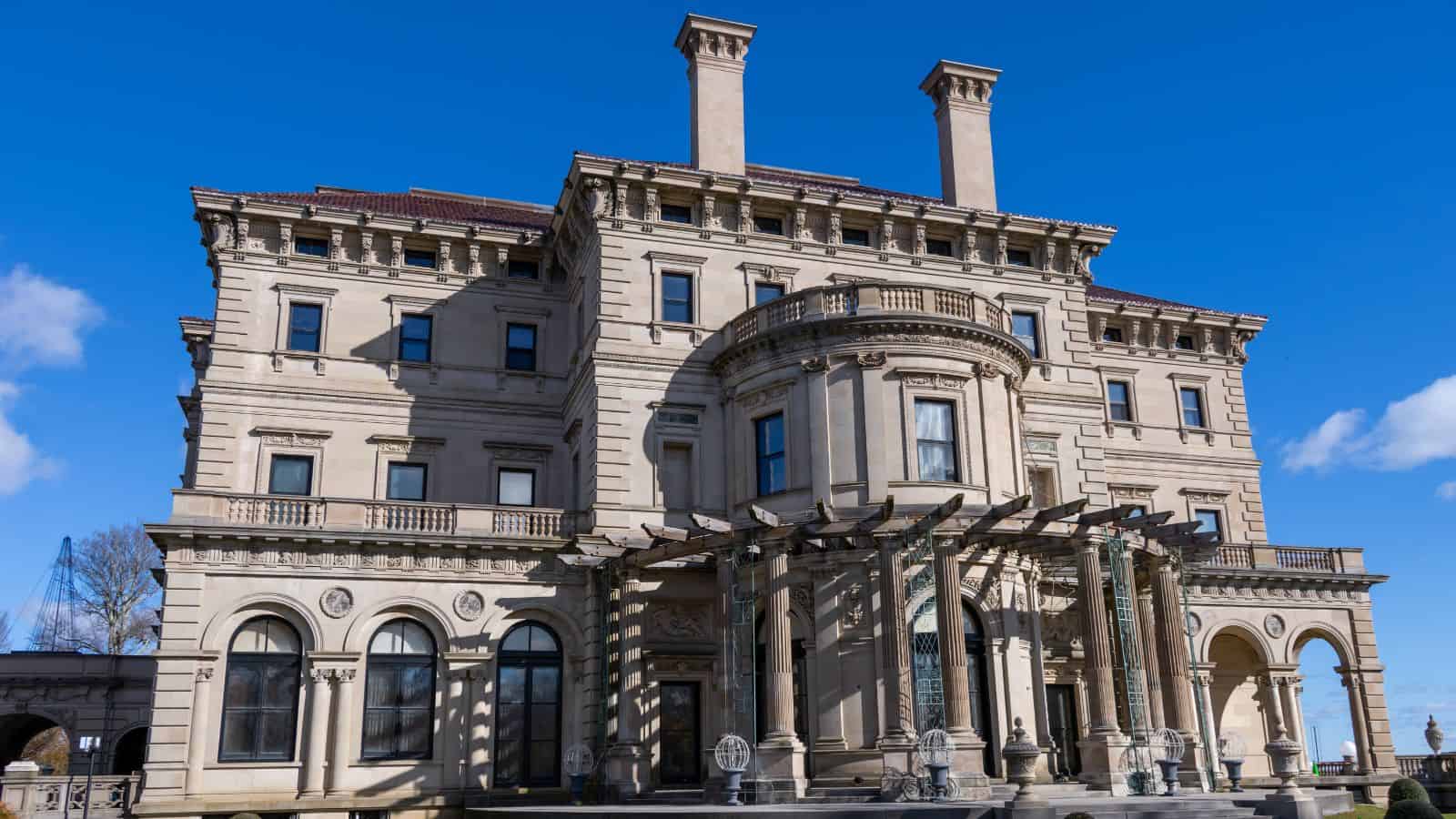 Large, ornate mansion with tall columns, arched windows, and detailed stonework under a clear blue sky.