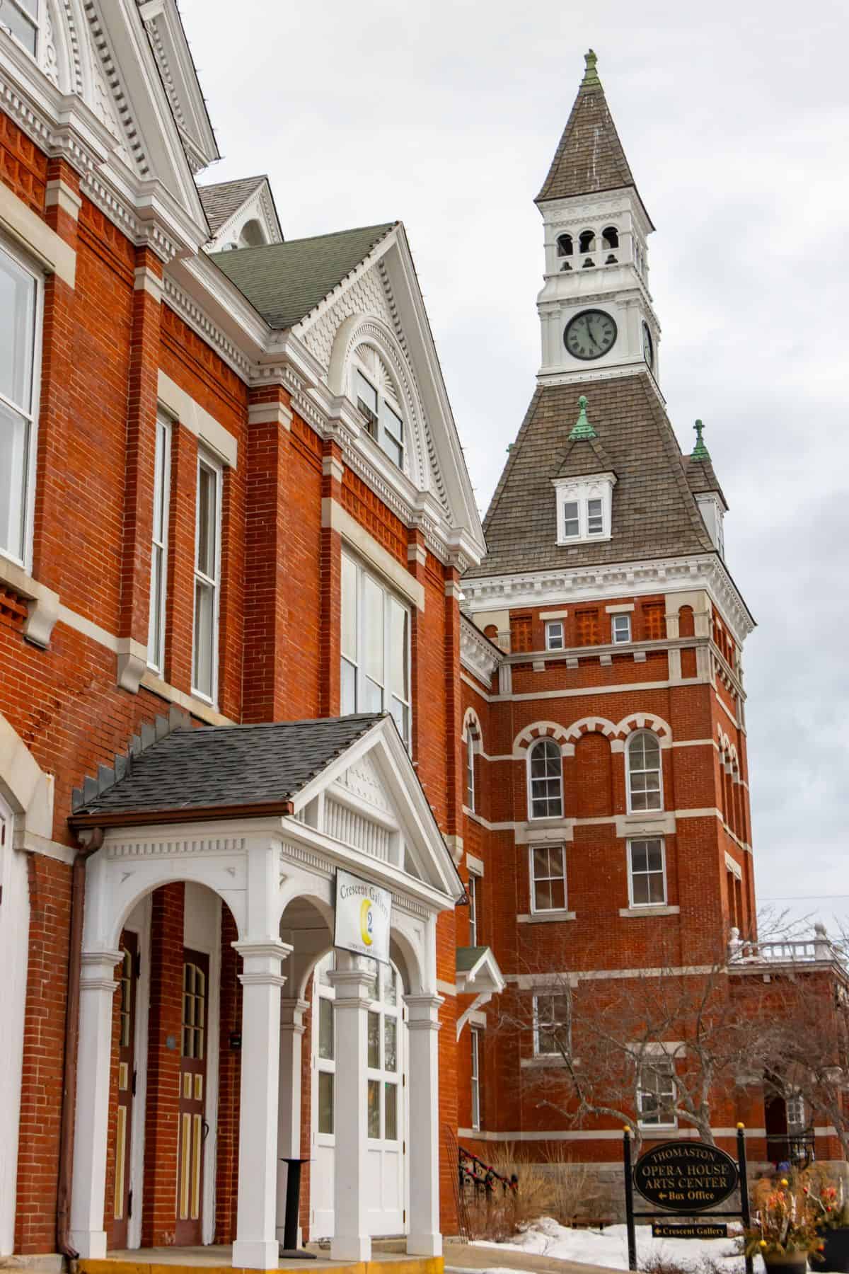 A historic red brick courthouse with a clock tower and arched windows, featuring white trim and a covered entrance, under a cloudy sky.