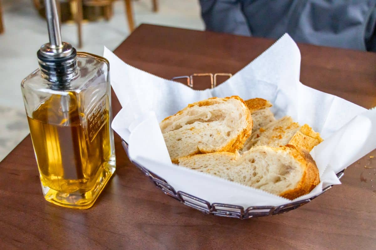 A basket of sliced bread on a table next to a glass bottle of olive oil.