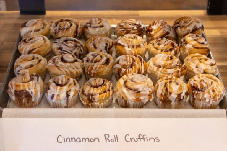 A tray of cinnamon roll cruffins with icing displayed on a wooden counter, labeled "Cinnamon Roll Cruffins.