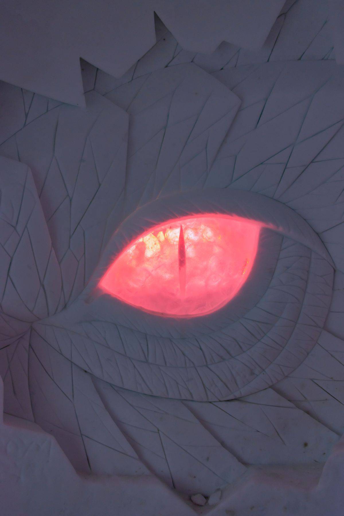 A glowing red, reptilian or dragon-like eye is set within a textured white surface, resembling scales or cracked stone.