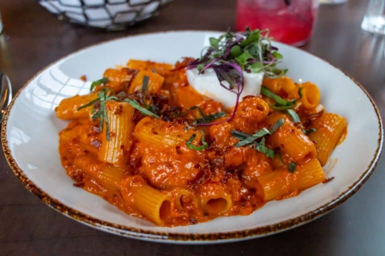 A plate of rigatoni pasta in a creamy tomato sauce, topped with fresh basil, microgreens, and a dollop of cheese.