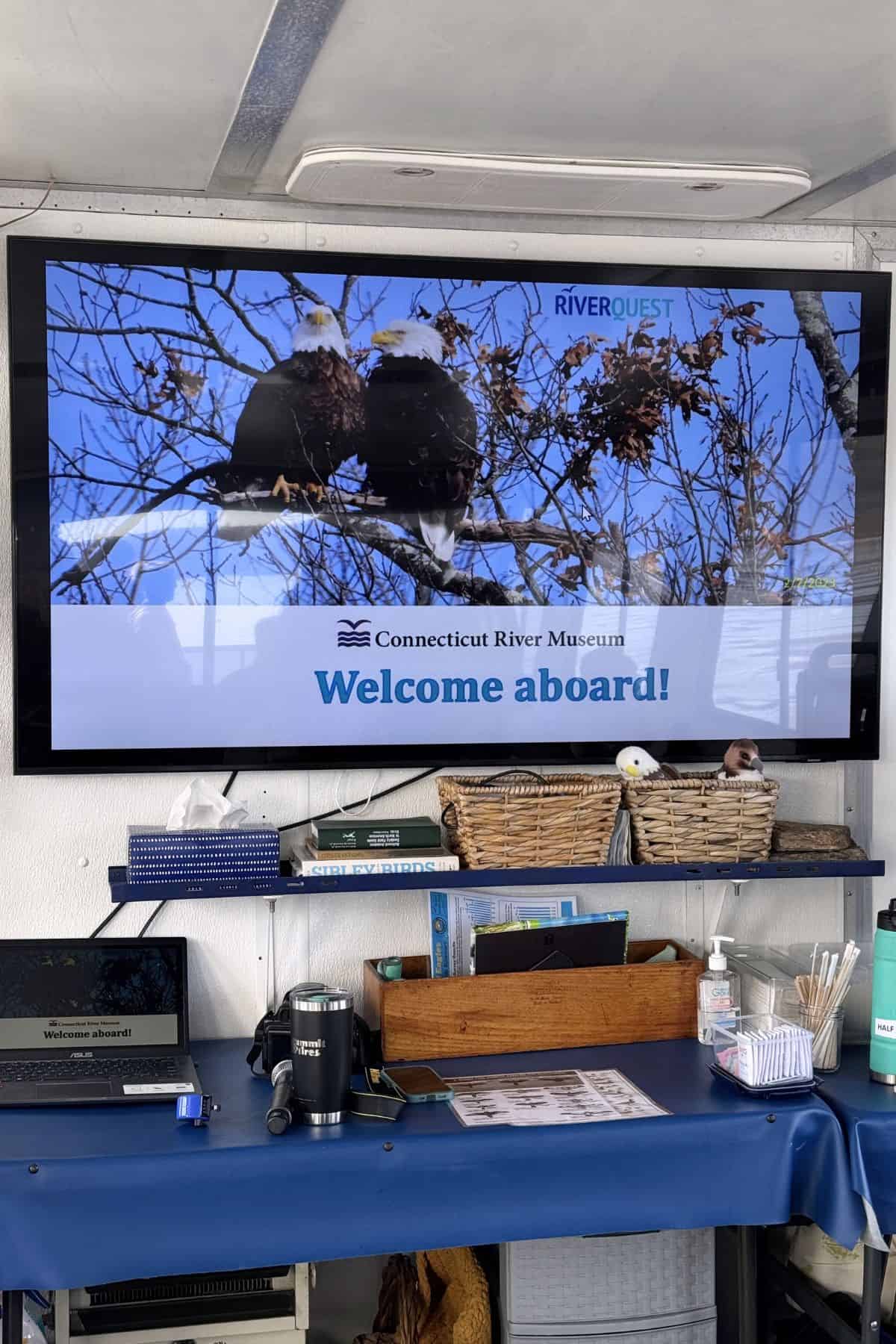 A display screen shows two bald eagles perched on a branch with the text "Connecticut River Museum Welcome aboard!" and various items on a blue table below.