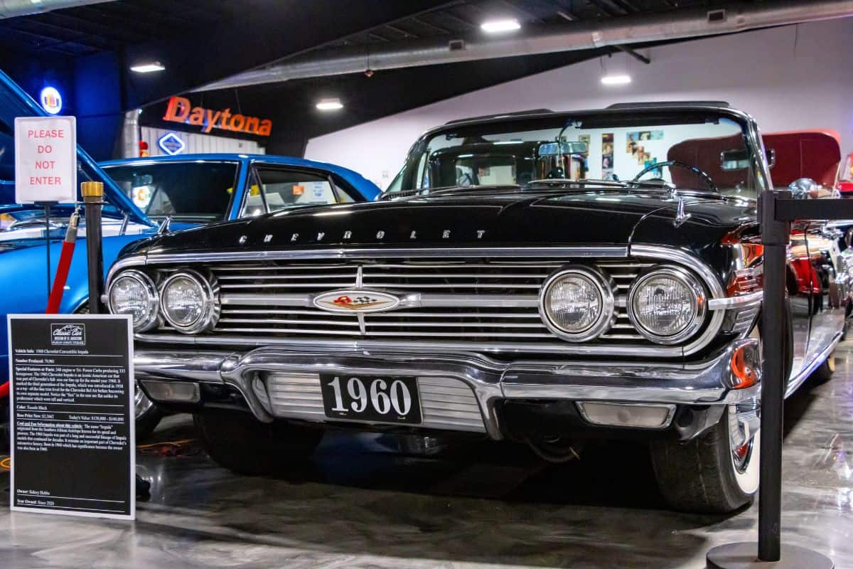 A 1960 black Chevrolet Impala on display in a car museum, positioned behind a barrier with informational signage in front.