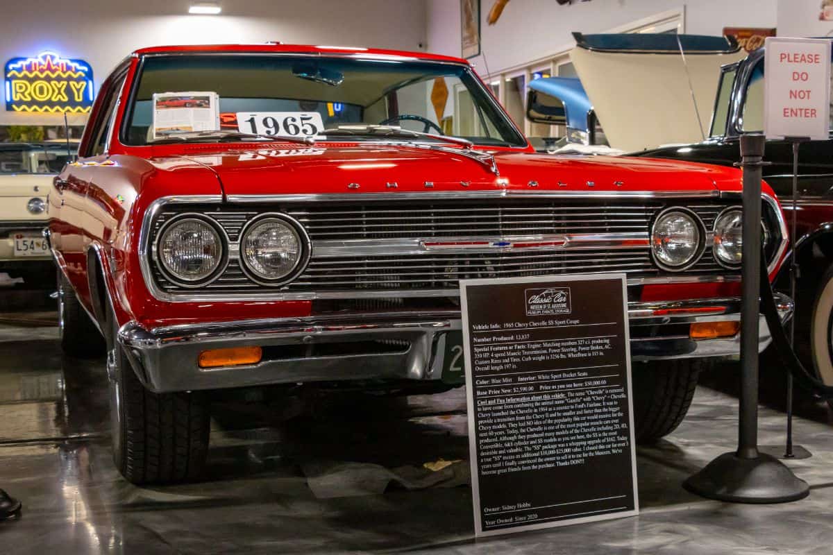 A red 1965 Chevrolet Chevelle Malibu on display in a museum, with an informational sign in front and a "Please Do Not Enter" sign nearby.