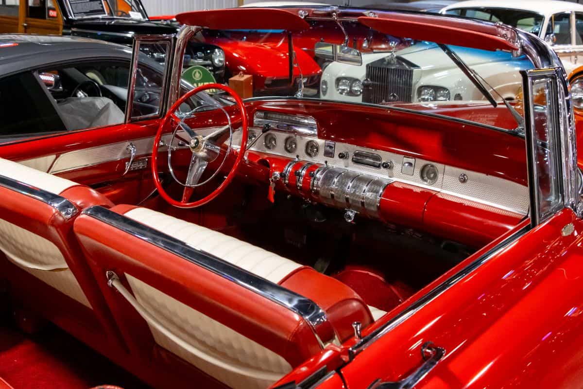 Interior of a classic red and white convertible car featuring a vintage dashboard, steering wheel, and front bench seat.