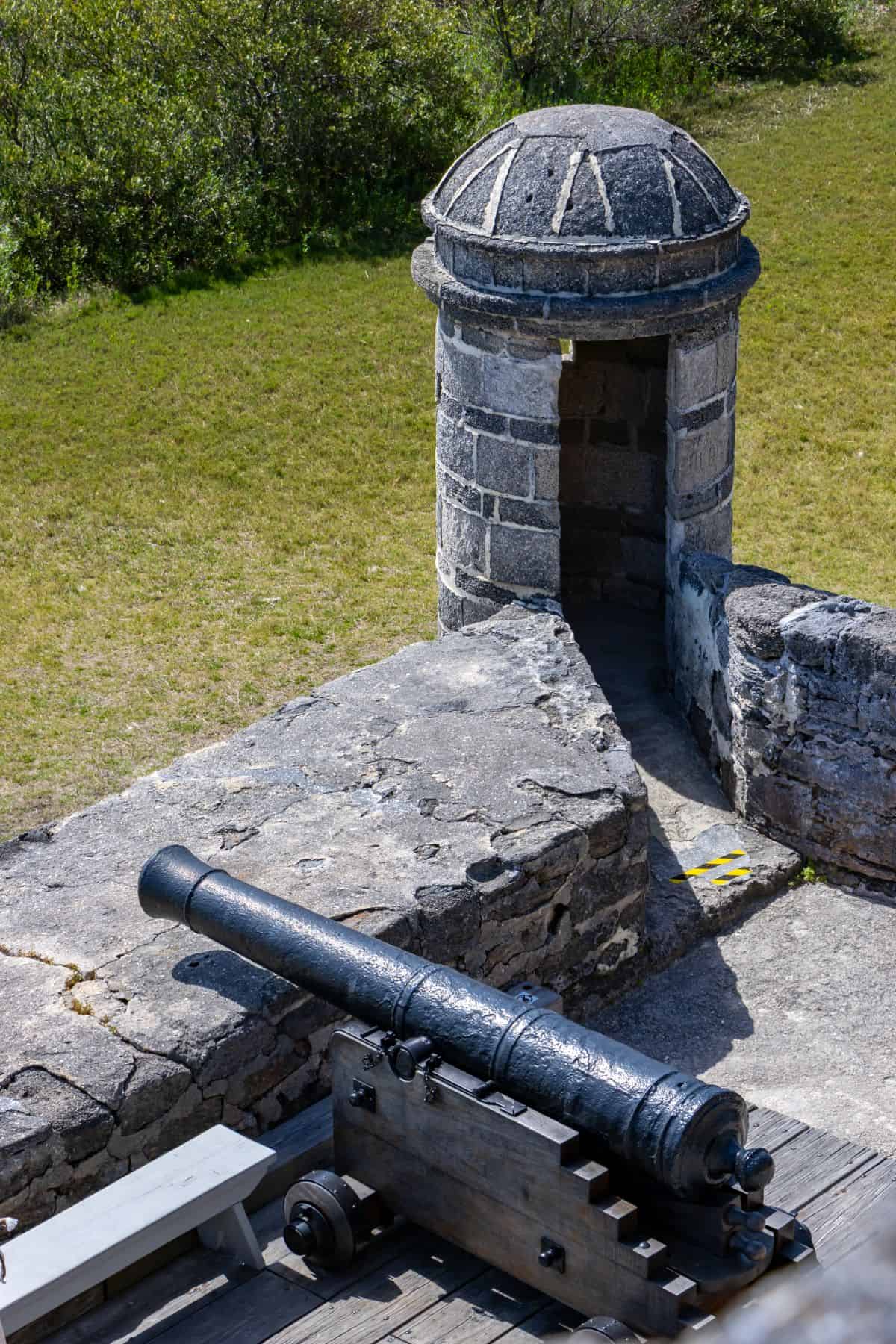 Historic cannon on a stone platform near a stone sentry box at Fort Matanzas National Monument, surrounded by grass and trees.