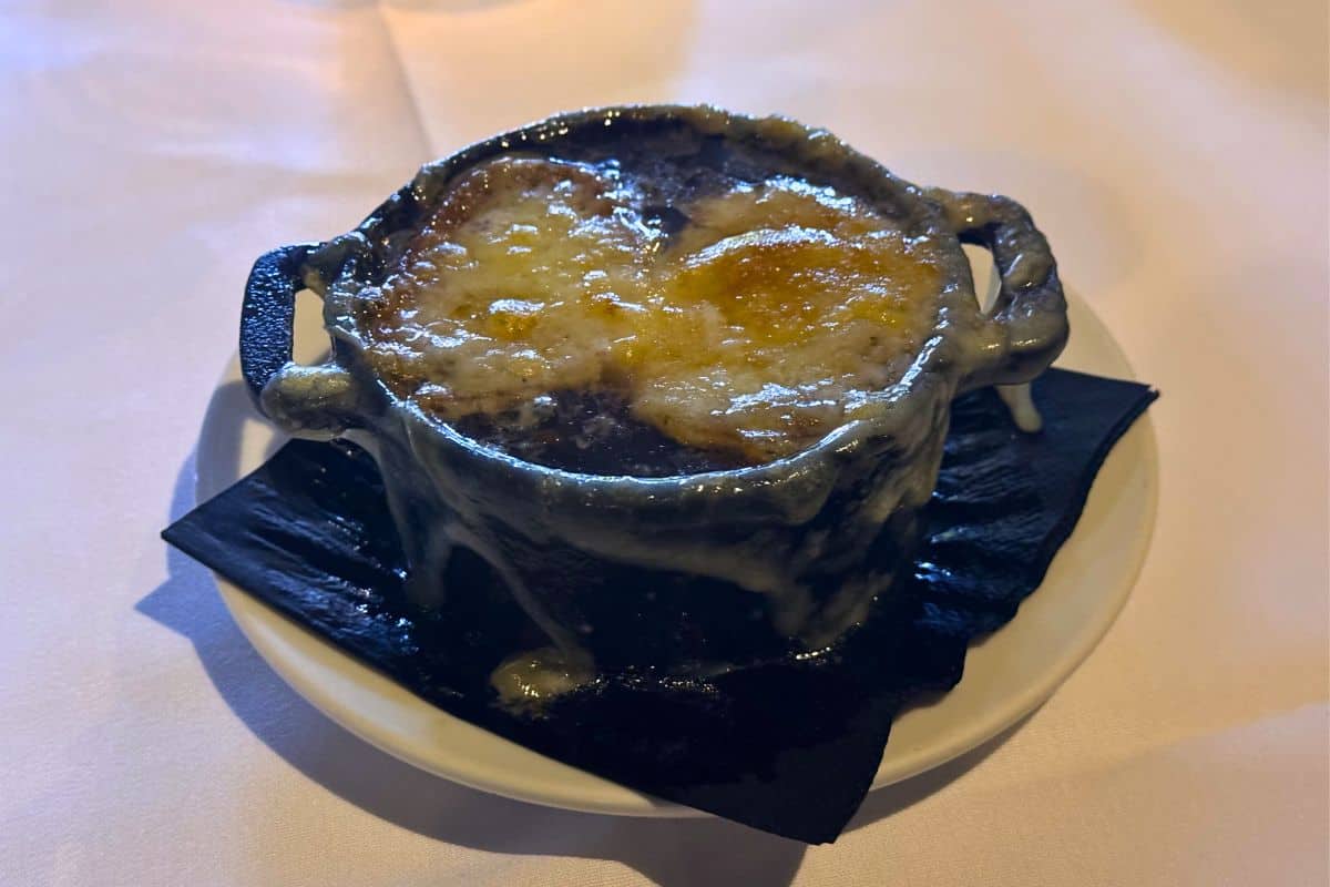 A small pot of French onion soup topped with melted, browned cheese, served on a white plate with a black napkin underneath.