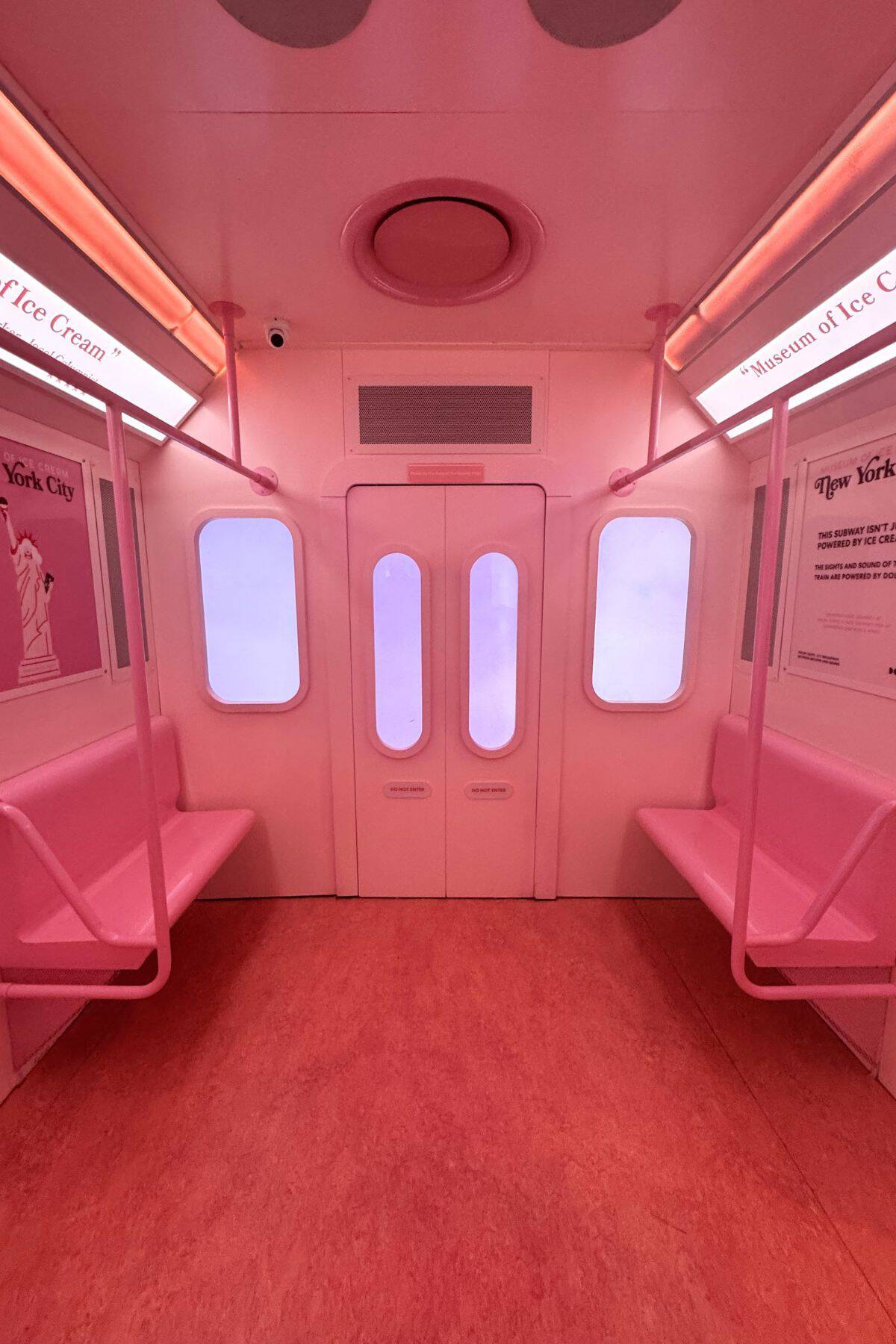 Empty subway car interior painted entirely pink, with pink seats, walls, and floor, and frosted windows. Signs above the seats reference the "Museum of Ice Cream.