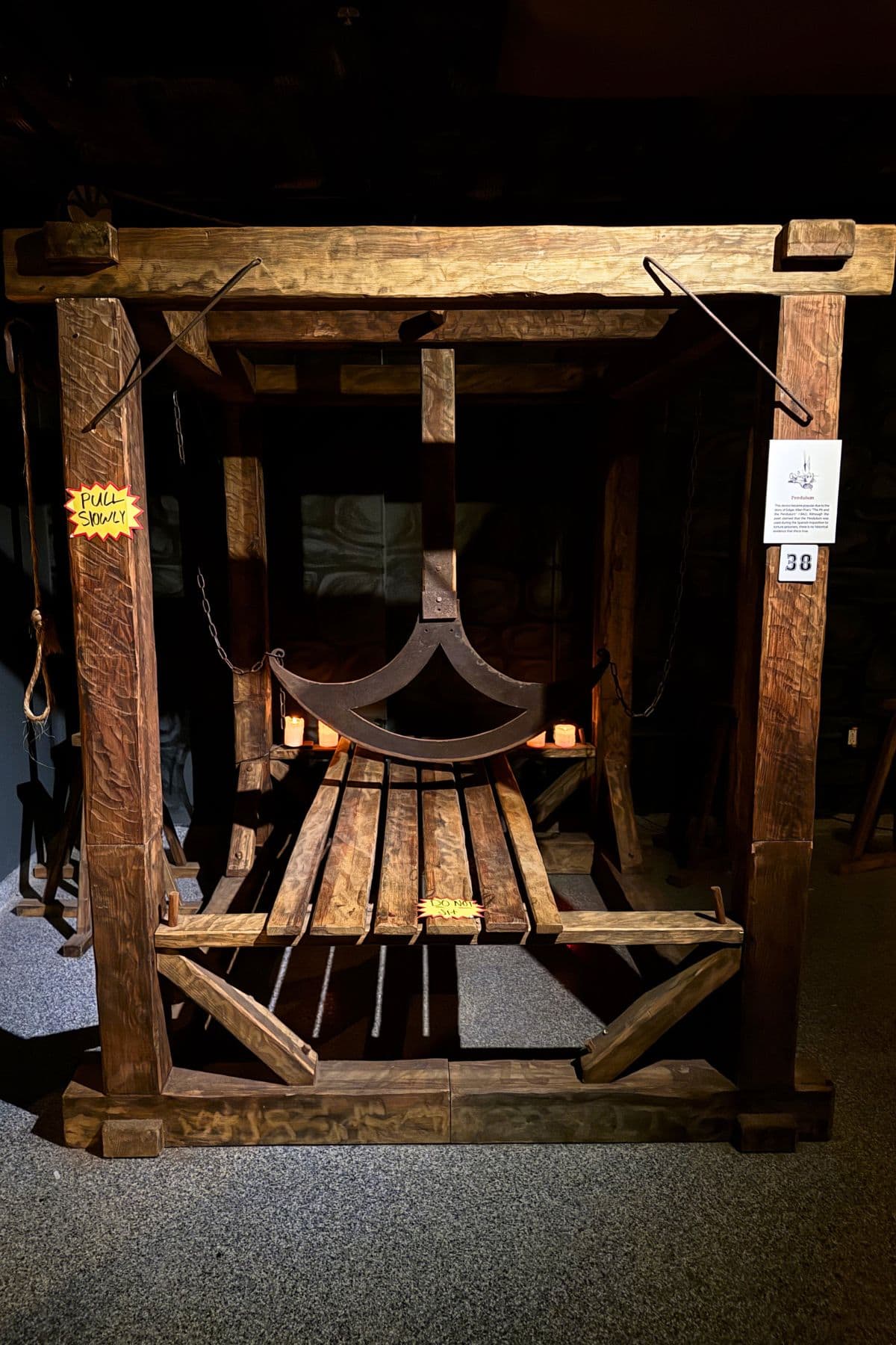 A large wooden medieval torture device with chains and slats, displayed indoors under dim lighting, with informational signs attached.