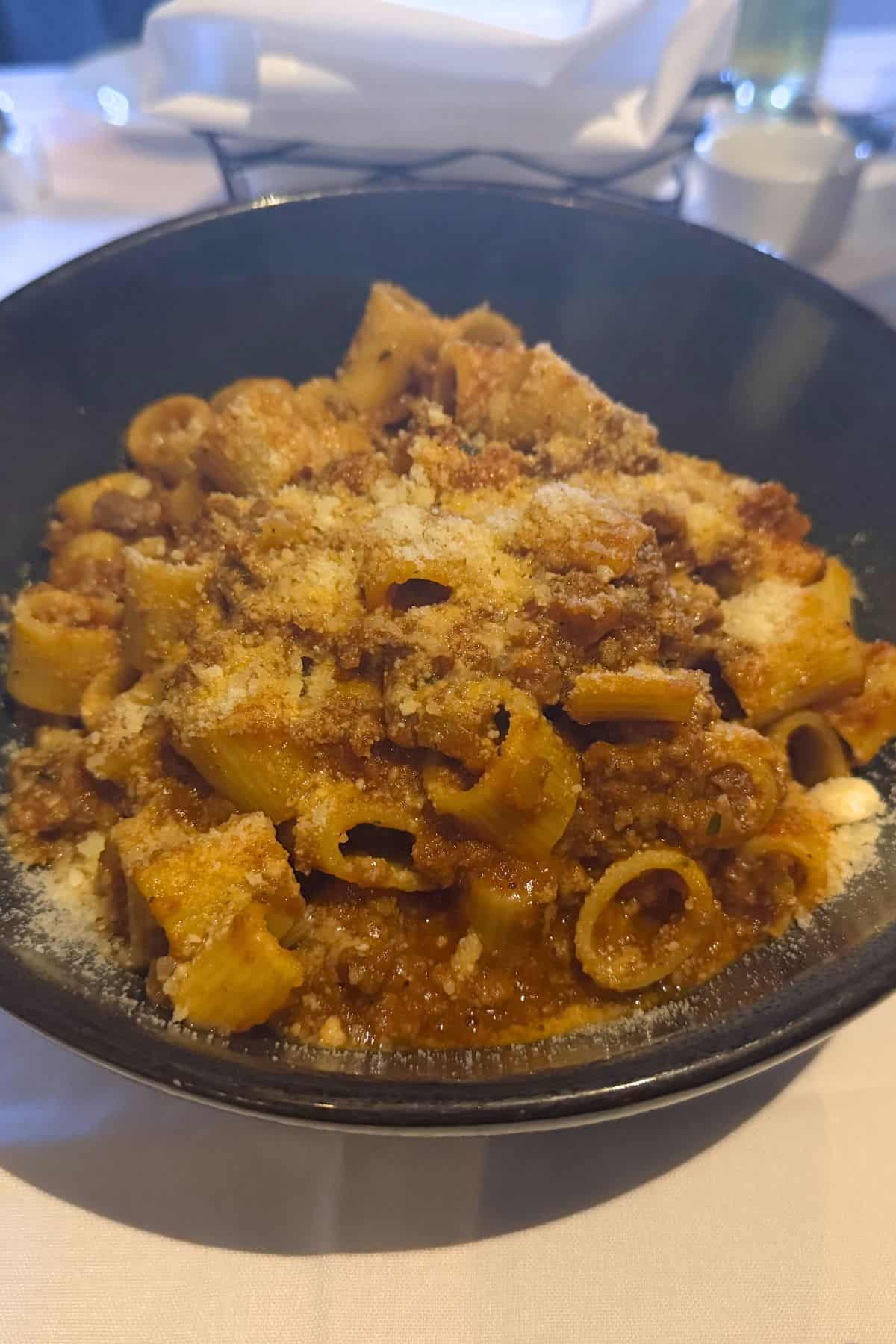 A black bowl filled with rigatoni pasta topped with a ground meat sauce and grated cheese.