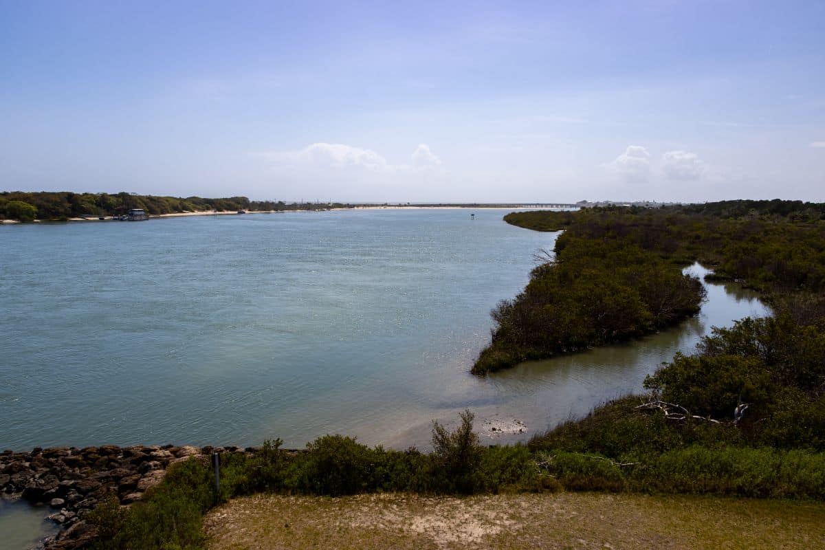 A wide river curves through green vegetation under a clear blue sky with some clouds on the horizon.
