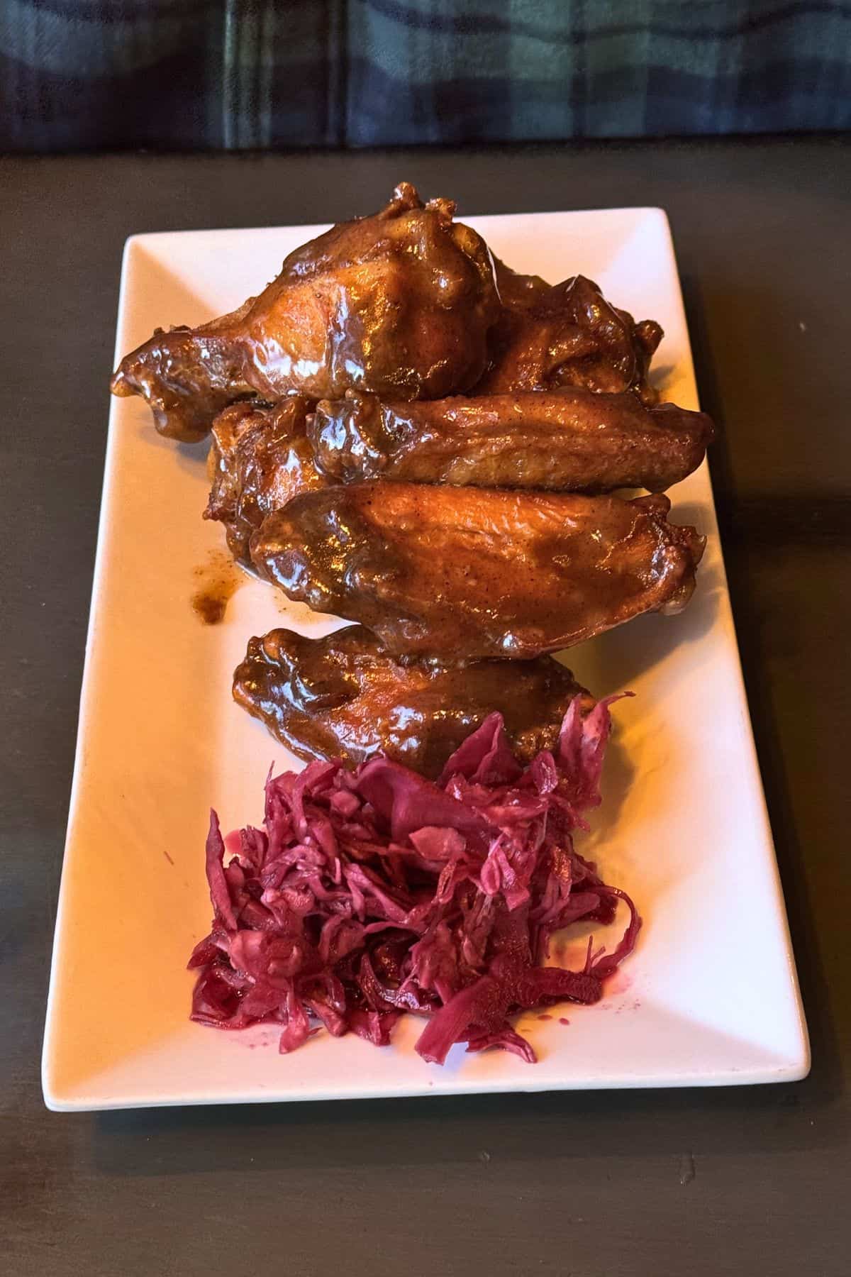 A rectangular white plate with barbecue-glazed chicken wings stacked next to a small serving of shredded red cabbage.