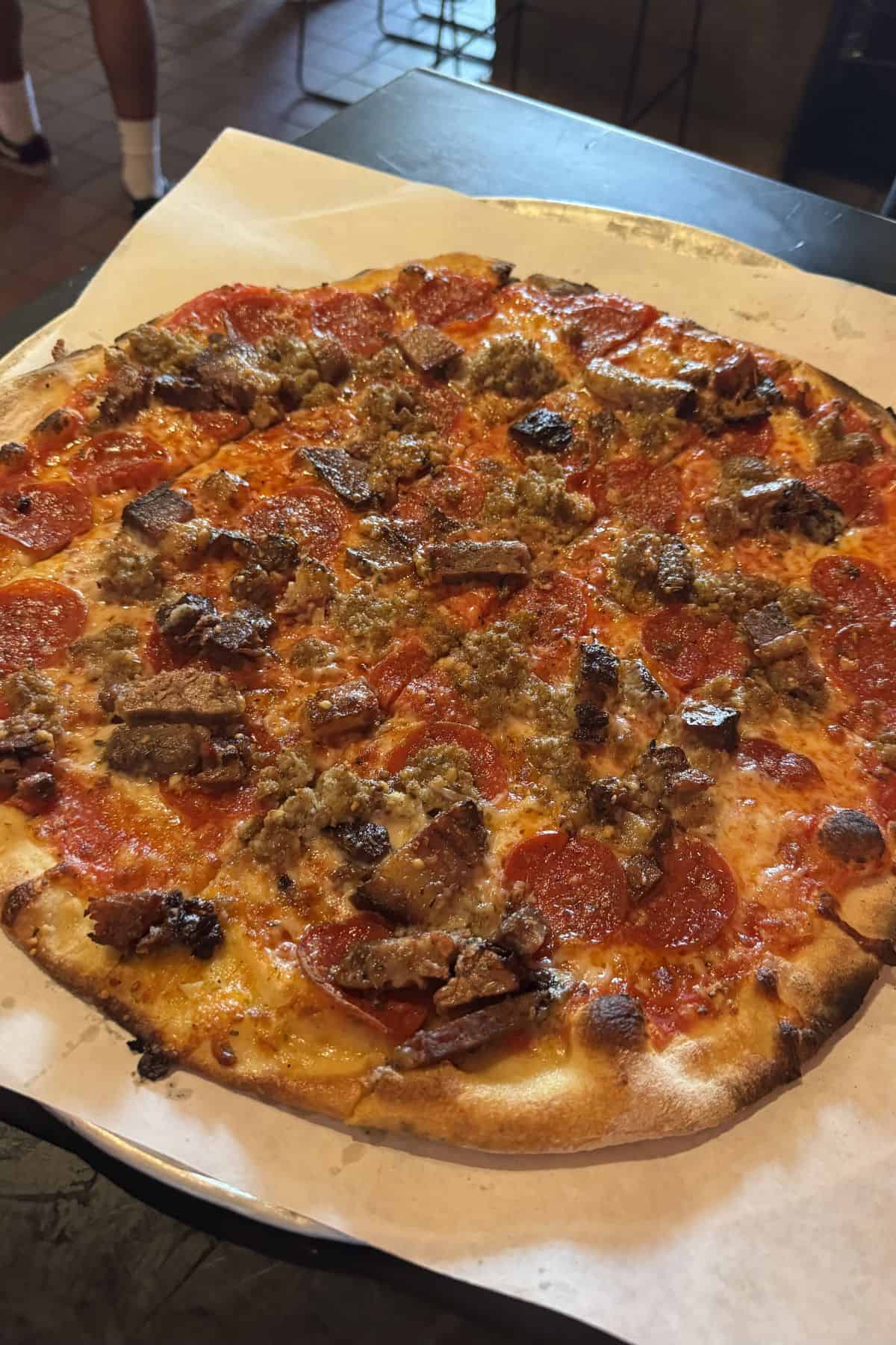 A cooked pizza topped with pepperoni, sausage, and pieces of beef on parchment paper.