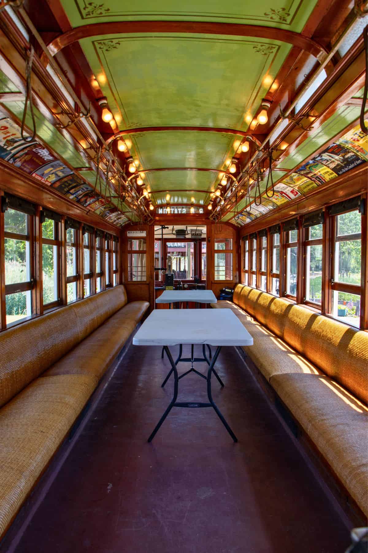 Interior of a vintage tram with long yellow benches, overhead lights, and a white folding table placed in the center aisle.
