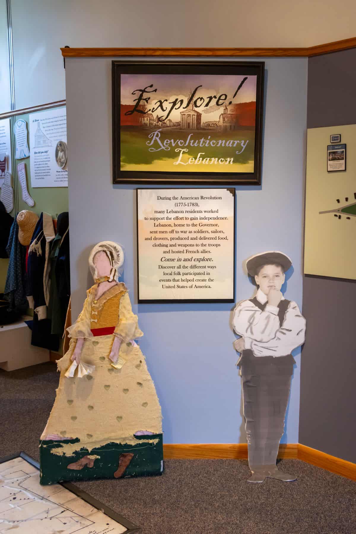 Exhibit display with a sign reading “Explore! Revolutionary Lebanon,” informational text, and two cardboard cutouts of a woman and a boy in period clothing.