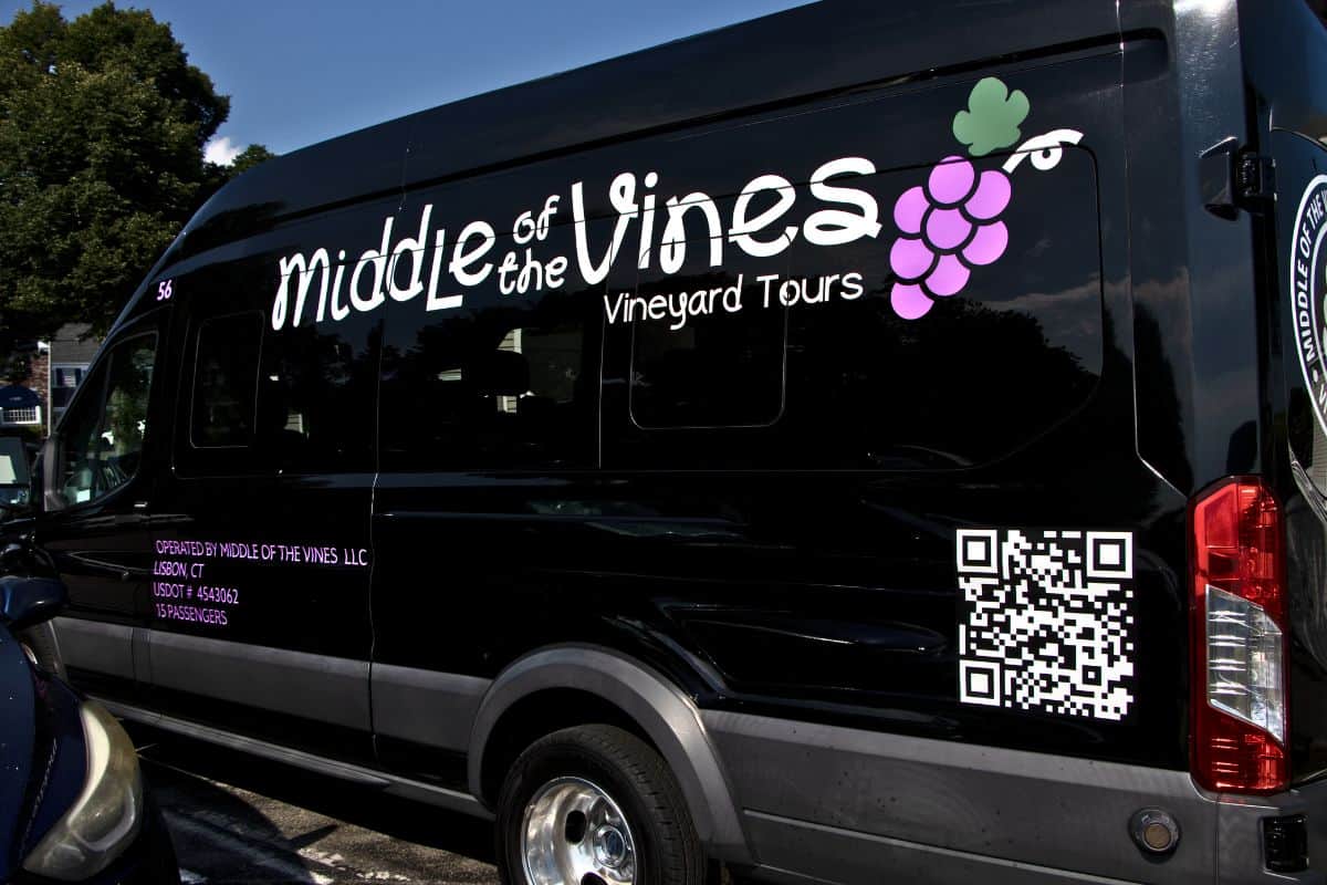 Black van with "Middle of the Vines Vineyard Tours" and a grape graphic on the side, along with a QR code and company information in white and purple text.