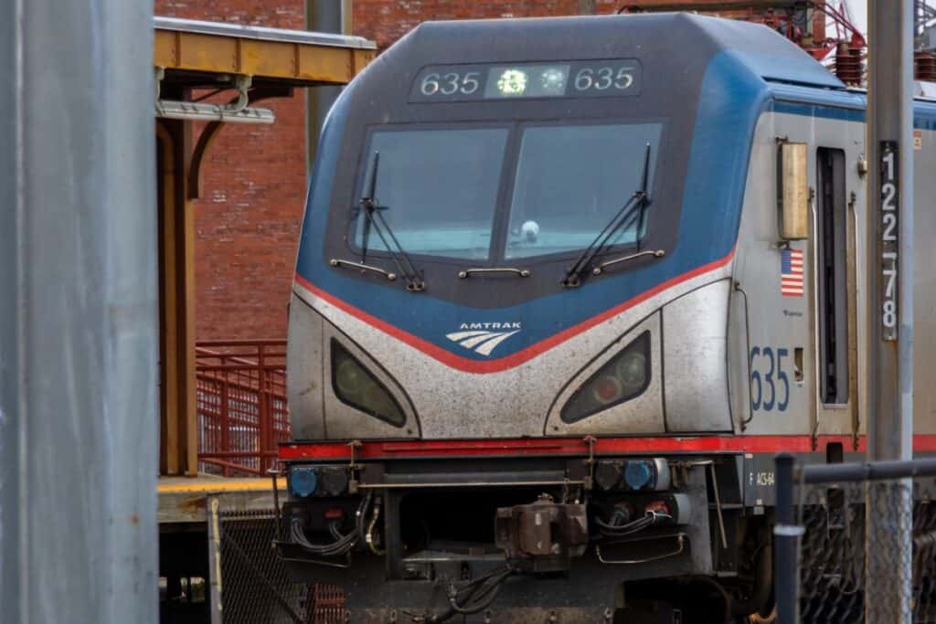 Close-up of the front of an Amtrak train at a station platform, showing train number 635 and American flag decal, with a brick building in the background.