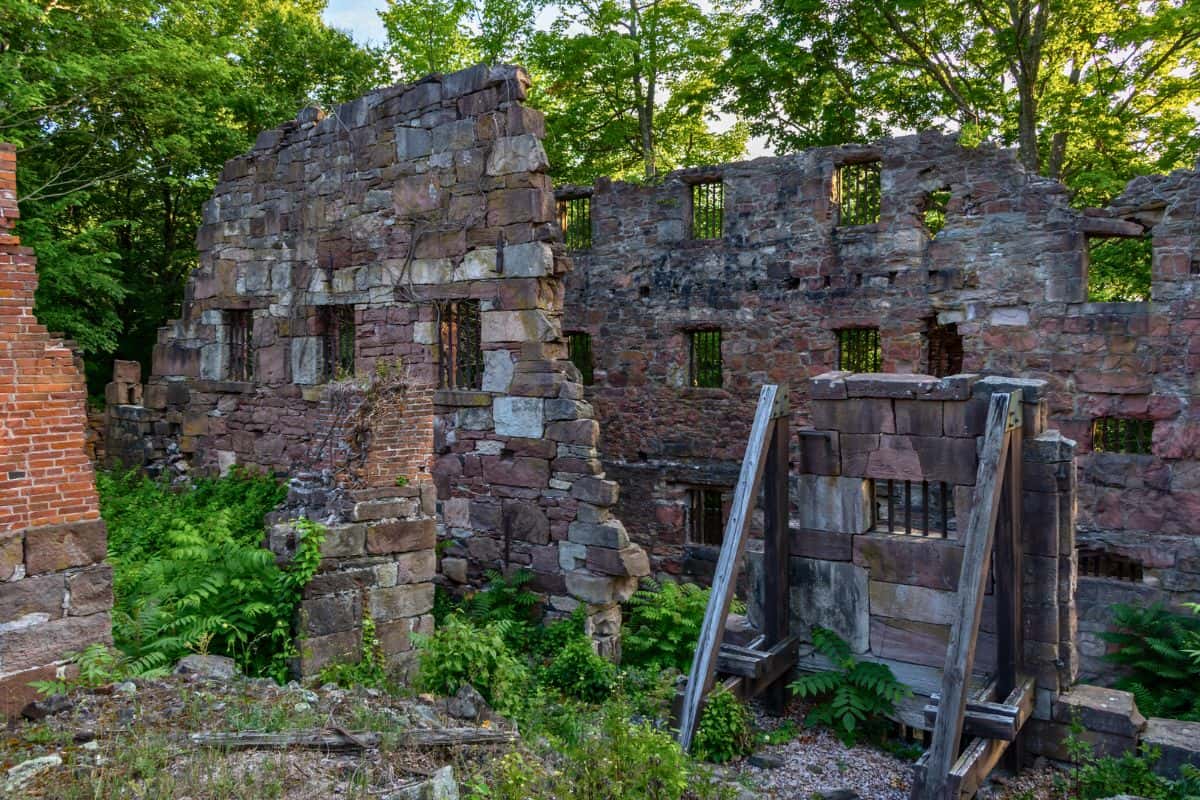 Stone and brick ruins of an old building with empty window openings, surrounded by green plants and trees, and partly supported by wooden beams.