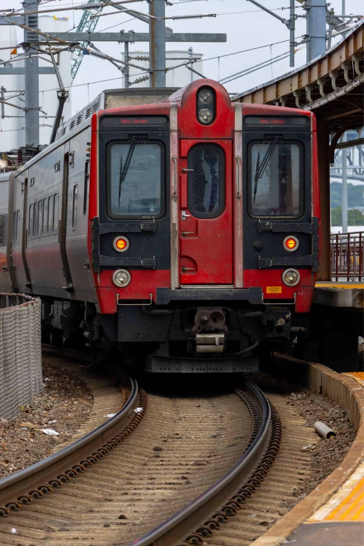 A red commuter train approaches a curved platform on tracks surrounded by overhead wires and infrastructure.