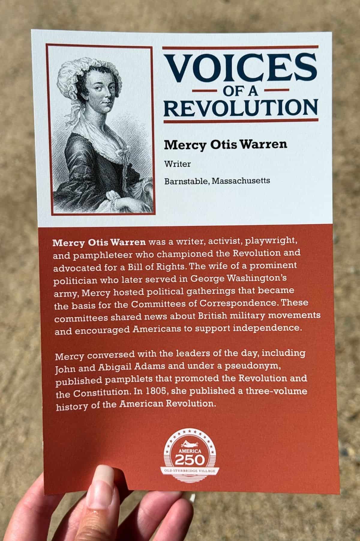 A person holds an informational card about Mercy Otis Warren, highlighting her role as a Revolutionary writer and pamphleteer, with a black-and-white portrait and descriptive text.