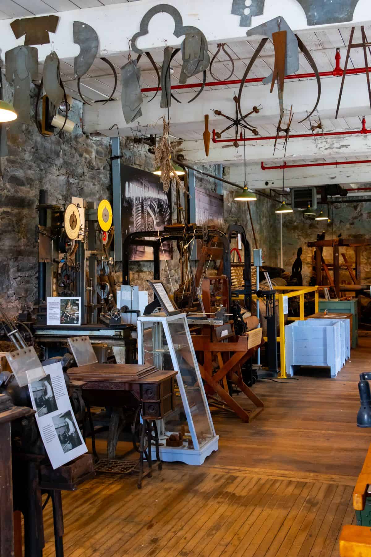 Room filled with vintage industrial machines, tools, and informational displays, set against stone walls and wooden floors in a museum-like setting.