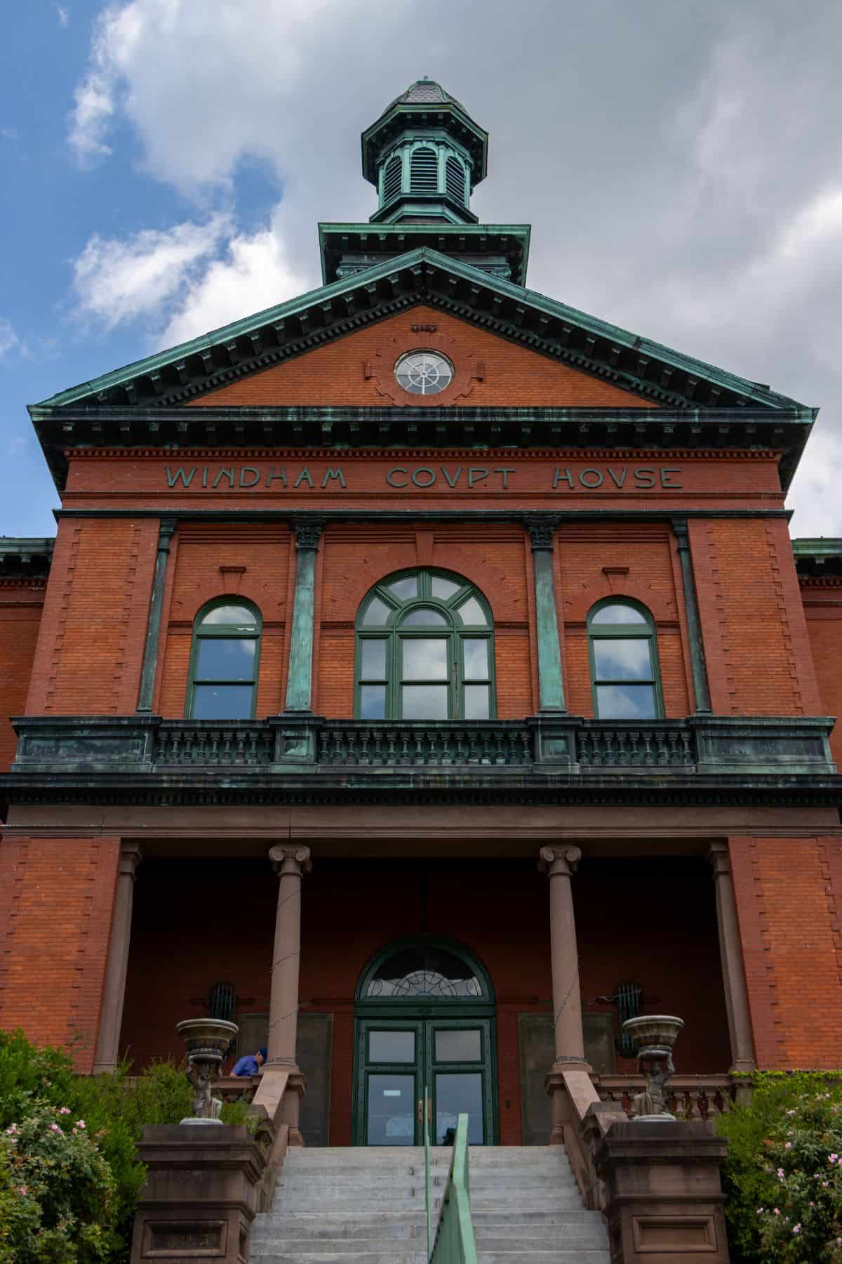 A brick courthouse building with green copper accents and a clock, labeled "WINDHAM COURT HOUSE," seen from the front steps under a partly cloudy sky.