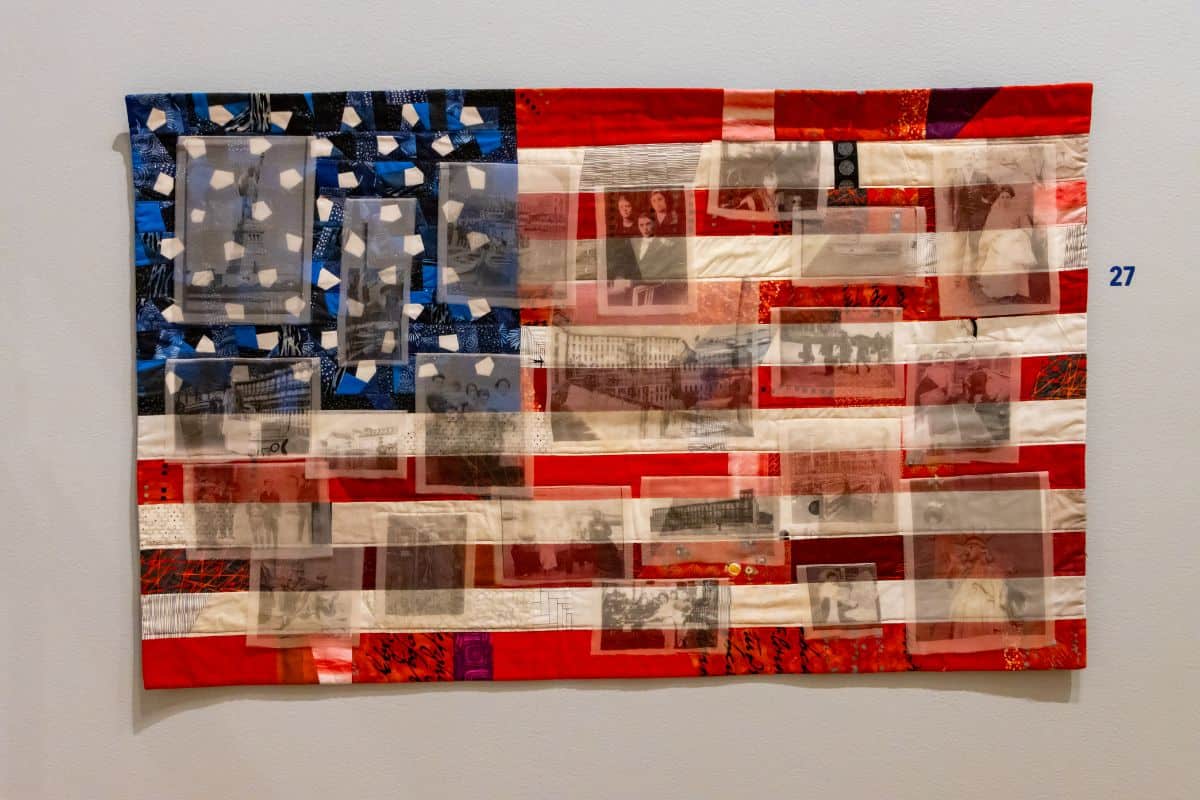 A quilt resembling the American flag, featuring red, white, and blue fabric with translucent sections displaying black-and-white photographs.
