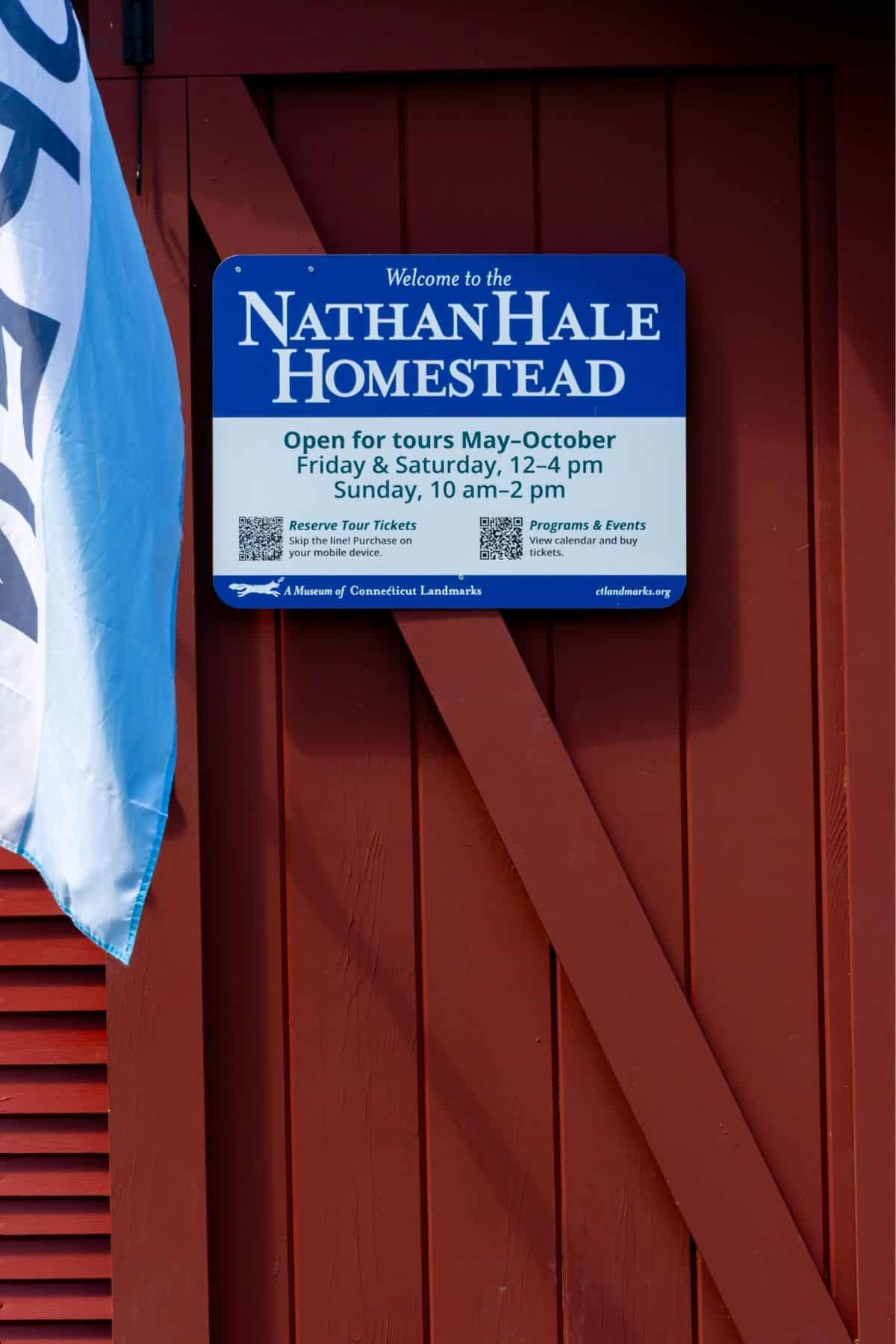 Sign on a red wooden wall displays Nathan Hale Homestead tour hours: Friday–Saturday 12–4 pm, Sunday 10 am–2 pm, May–October. Includes info about tickets and programs.