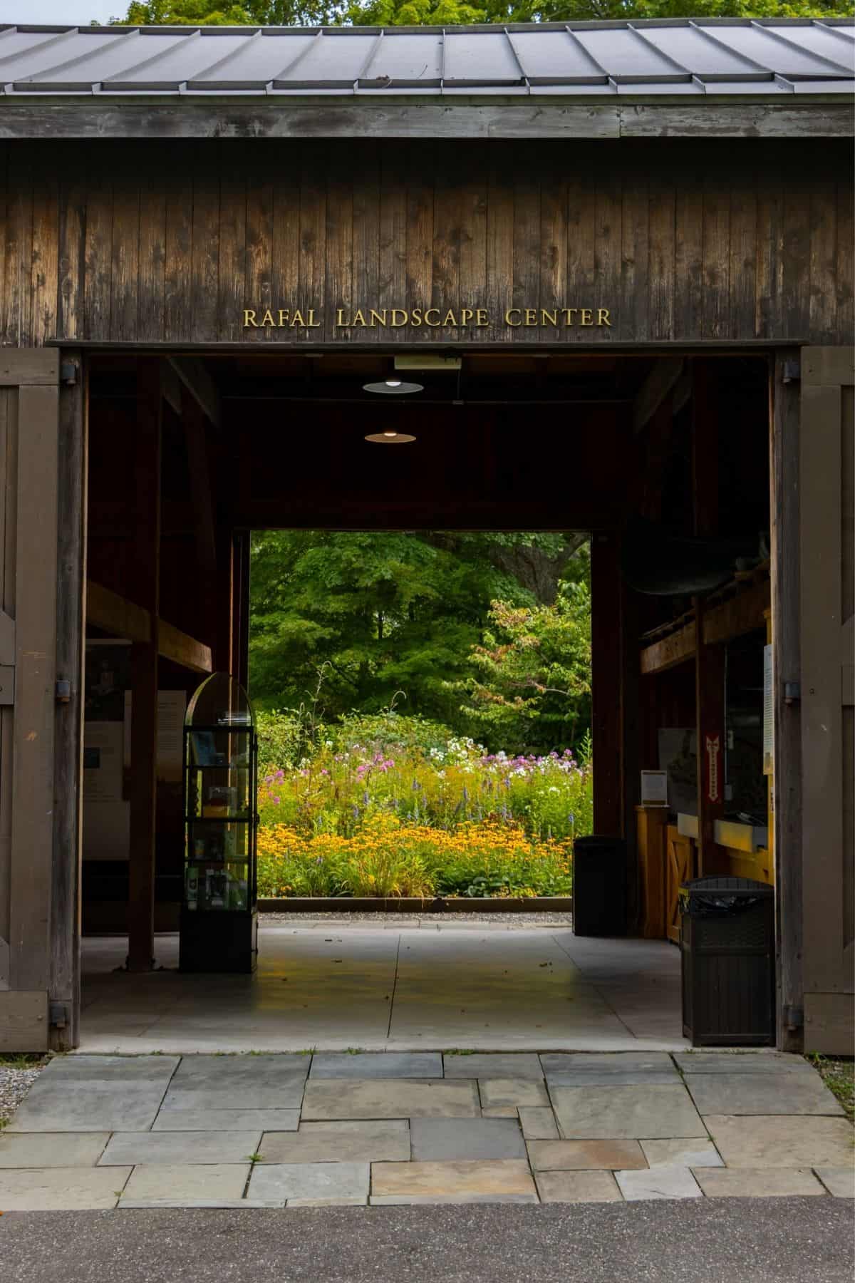 Entrance to the Rafal Landscape Center, with an open doorway leading to a colorful garden and trees in the background.