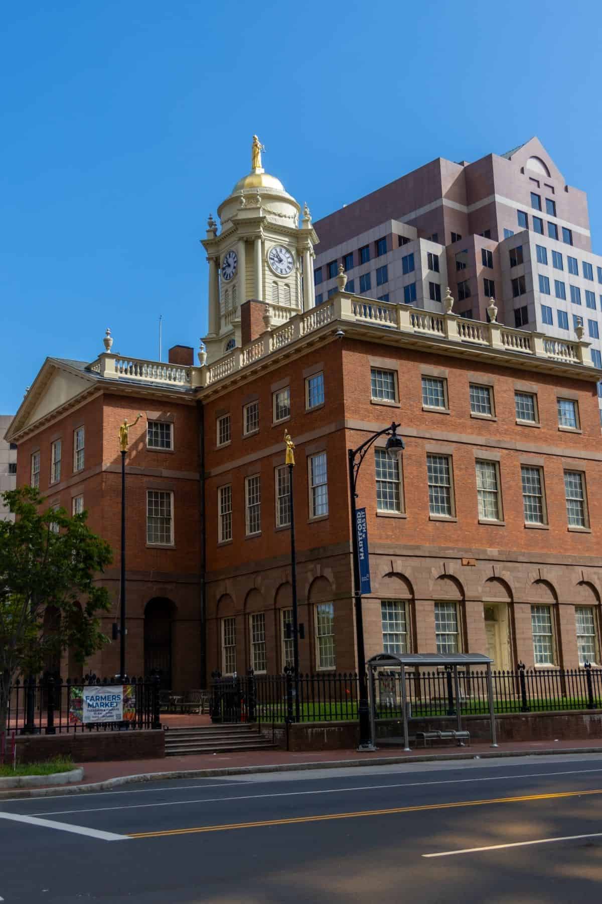 Historic brick building with a clock tower, surrounded by modern office buildings, under a clear blue sky.