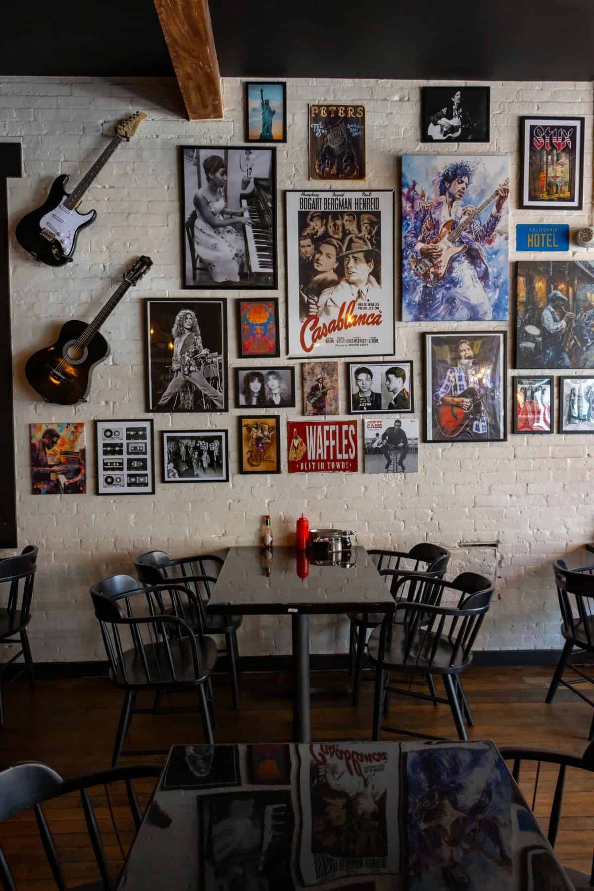 A gallery wall of music and movie posters and two guitars hanging above black dining tables and chairs.